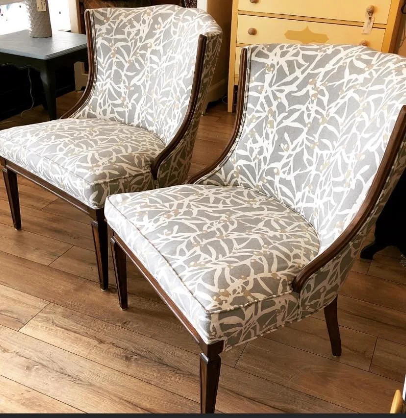 Two upholstered armchairs with wooden frames and patterned fabric in a room with a hardwood floor and nearby furniture.