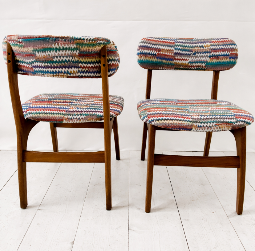 Two wooden chairs with colorful, patterned upholstery on the seats and backs, set against a white background on a white floor.