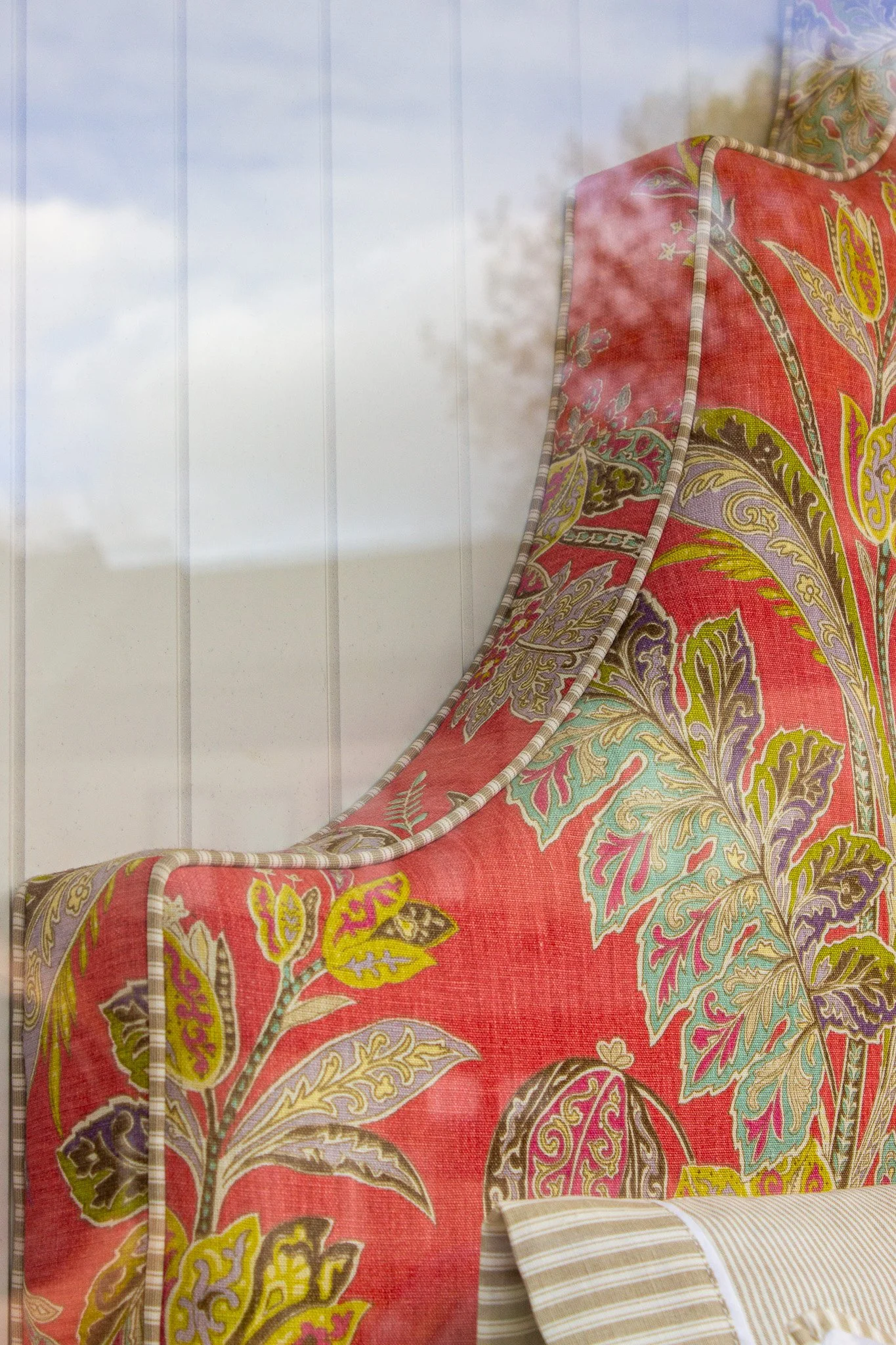 Close-up of a floral-patterned headboard or furniture piece with a pink background and green, yellow, and purple leaves, reflected in a glass window.