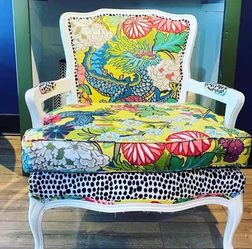 A vintage-style white wooden armchair with colorful Asian-inspired dragon and floral upholstery, including a dragon motif on the backrest and a polka dot pattern on the seat skirt.