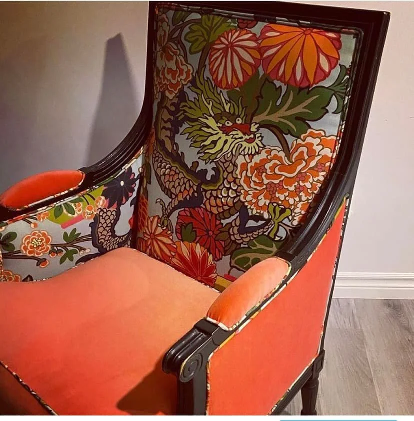 A decorative armchair with a vibrant dragon and floral pattern on the backrest and a solid orange seat cushion.
