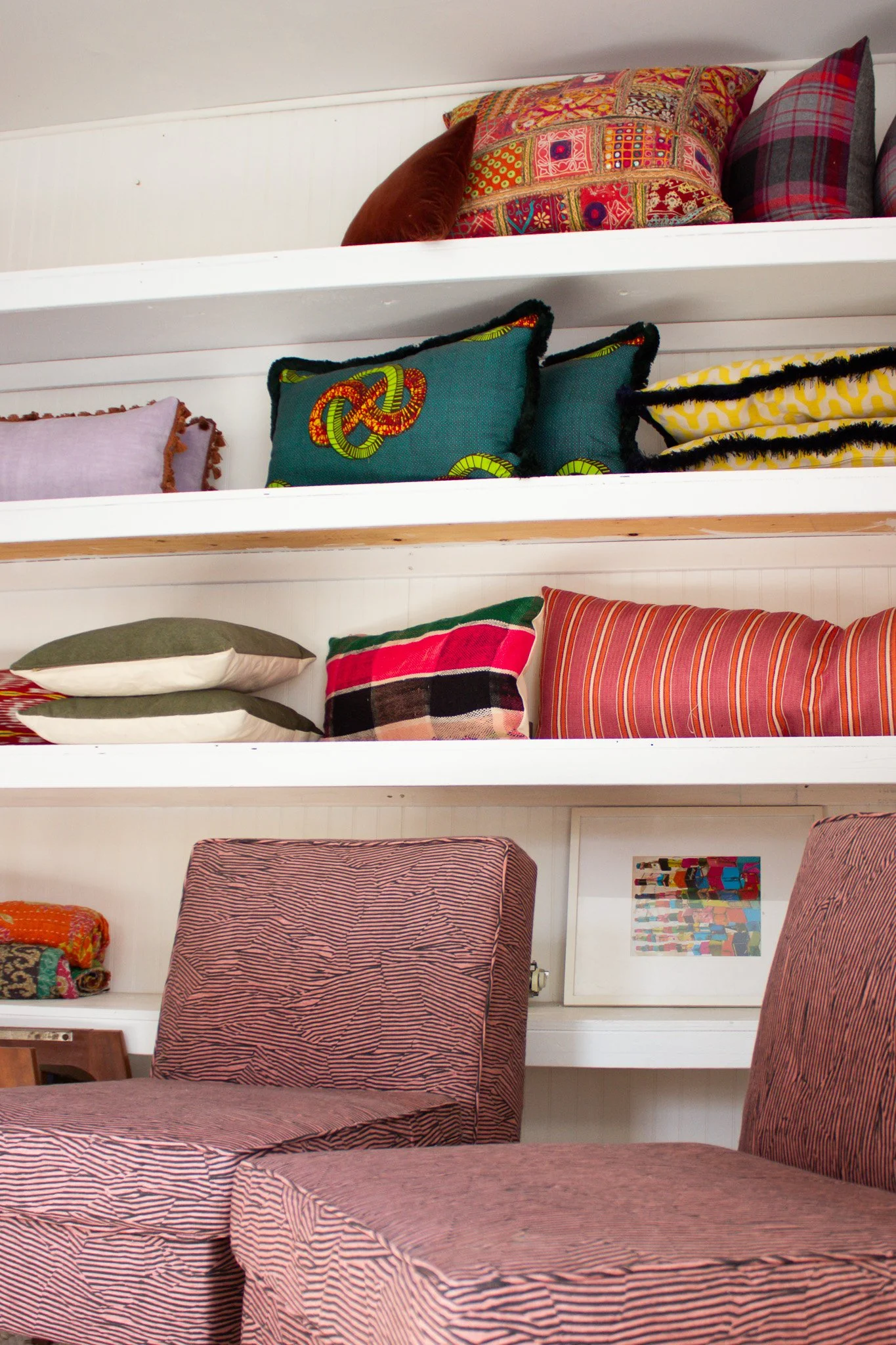 Shelves filled with colorful pillows and blankets in a showroom, with two upholstered chairs in front.