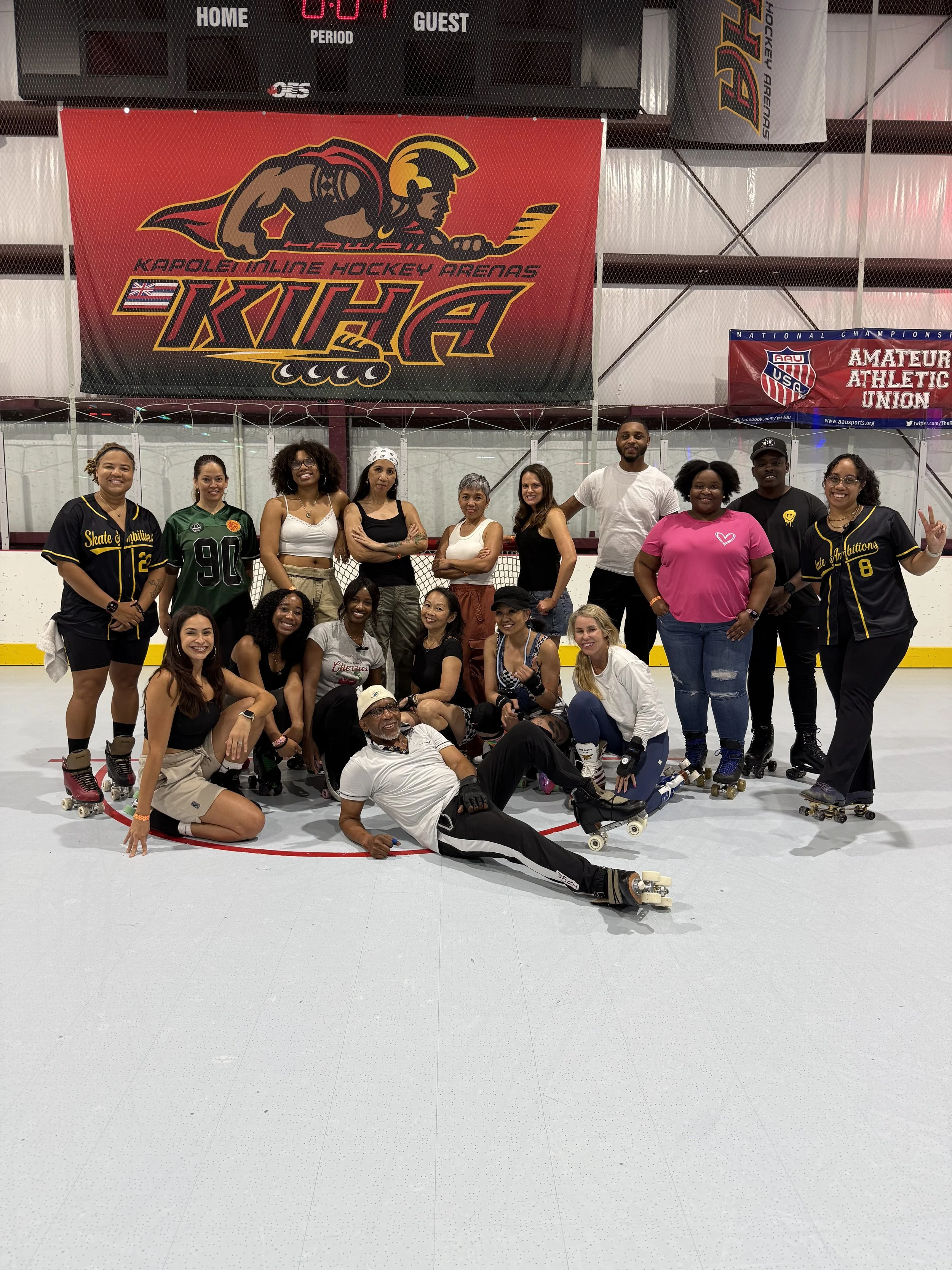 Group of people posing on an indoor roller skating rink, with a large red banner for Kapolei Inline Hockey Arenas (KIHA) and a smaller banner for Amateur Athletic Union (AAU) in the background.