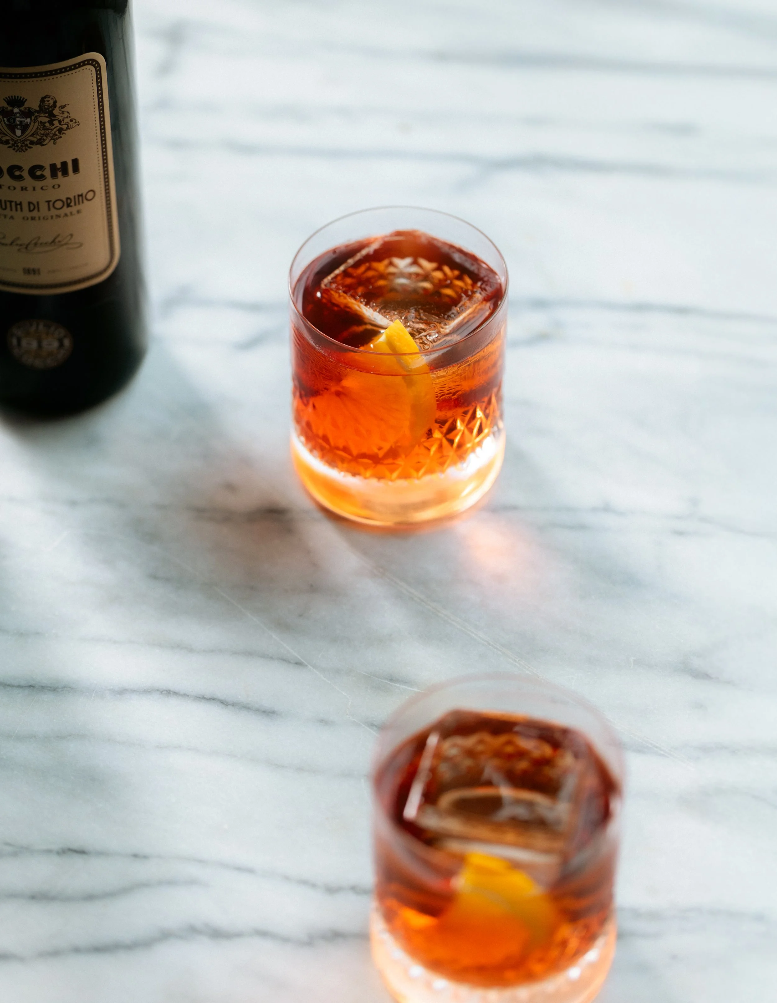 A glass of iced tea with lemon slices on a marble table, and a bottle of liquor partially visible on the left side.