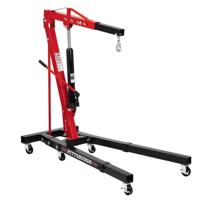 A red and black portable engine hoist or cherry picker with several caster wheels, a hydraulic pump, and an adjustable boom for lifting engines or heavy objects.