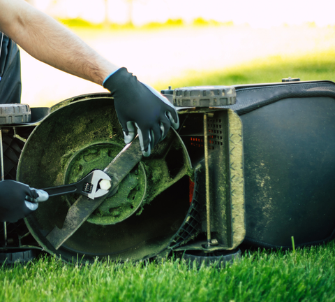 A person tightening a lawn mower blade with a wrench.