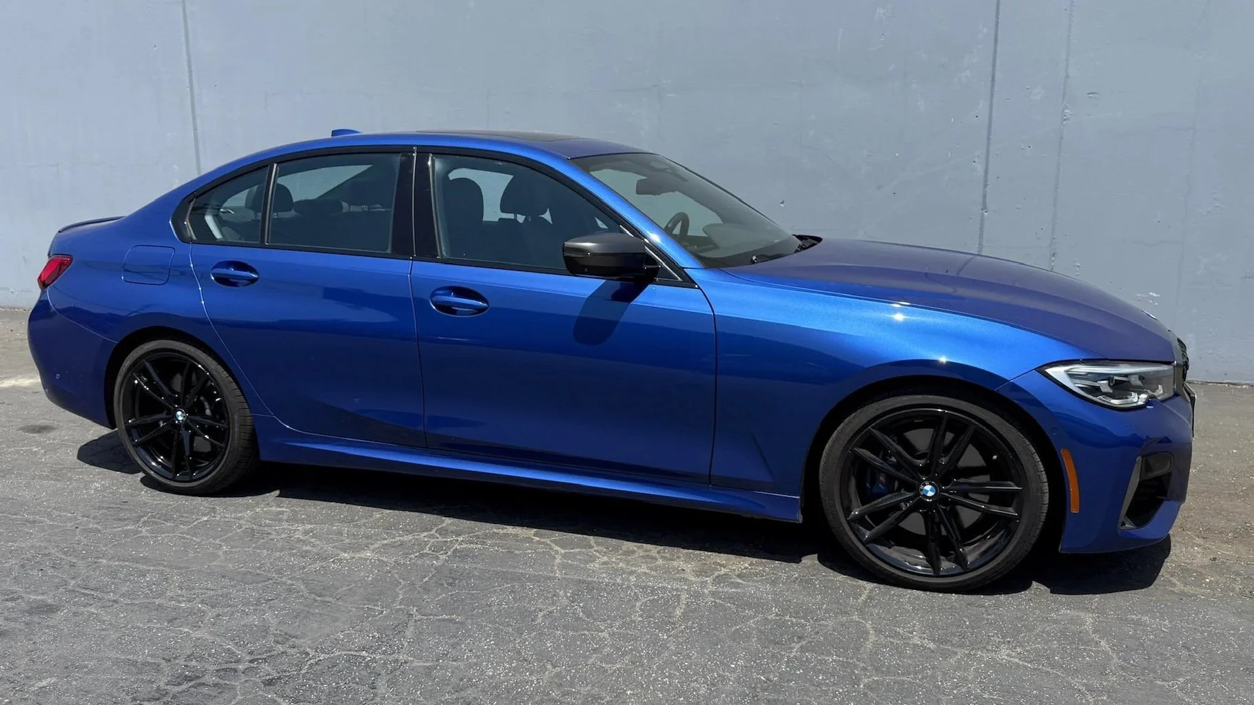 A blue BMW sedan parked on a paved surface against a gray wall.
