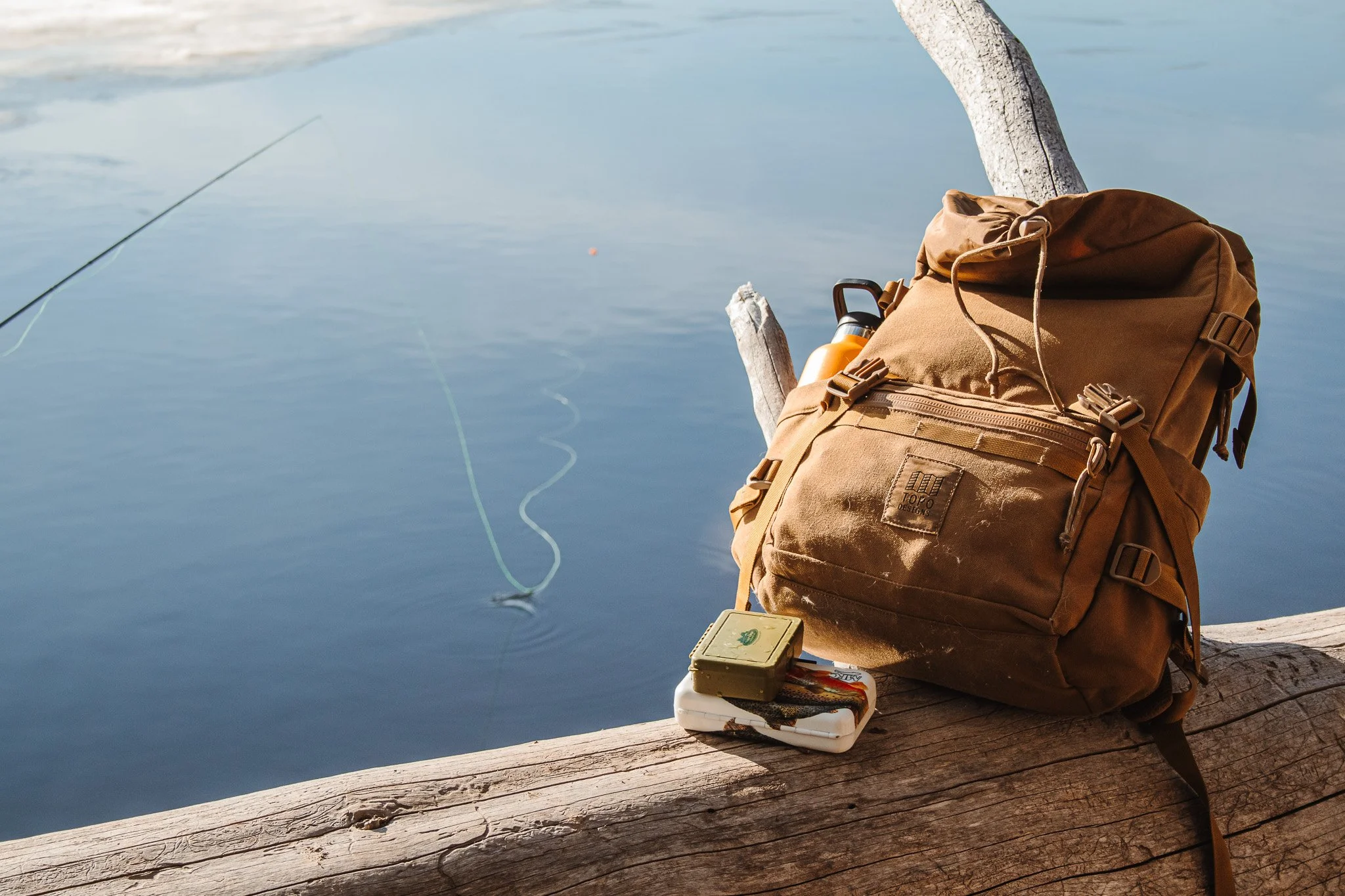 Brown backpack resting on a log beside calm water during an outdoor adventure.