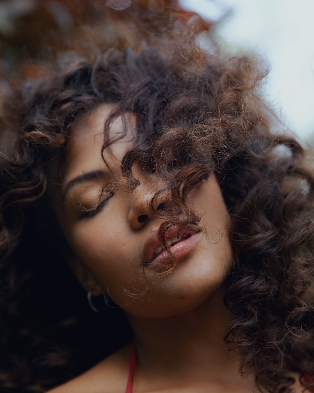Close-up of a woman with curly hair and closed eyes, slightly parted lips, and wearing hoop earrings.