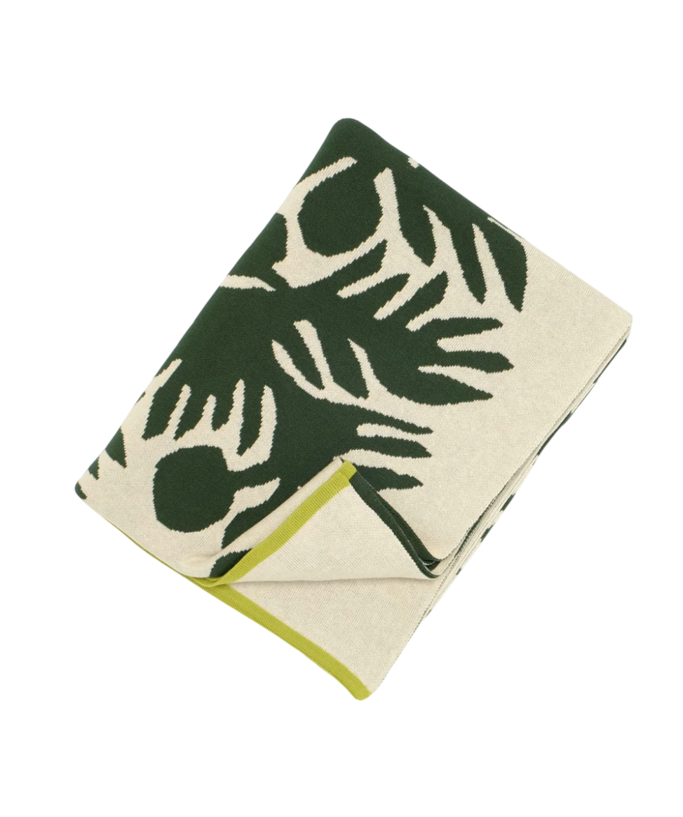 A folded towel with a green and white tropical leaf pattern, edged with lime green, placed on a black surface.