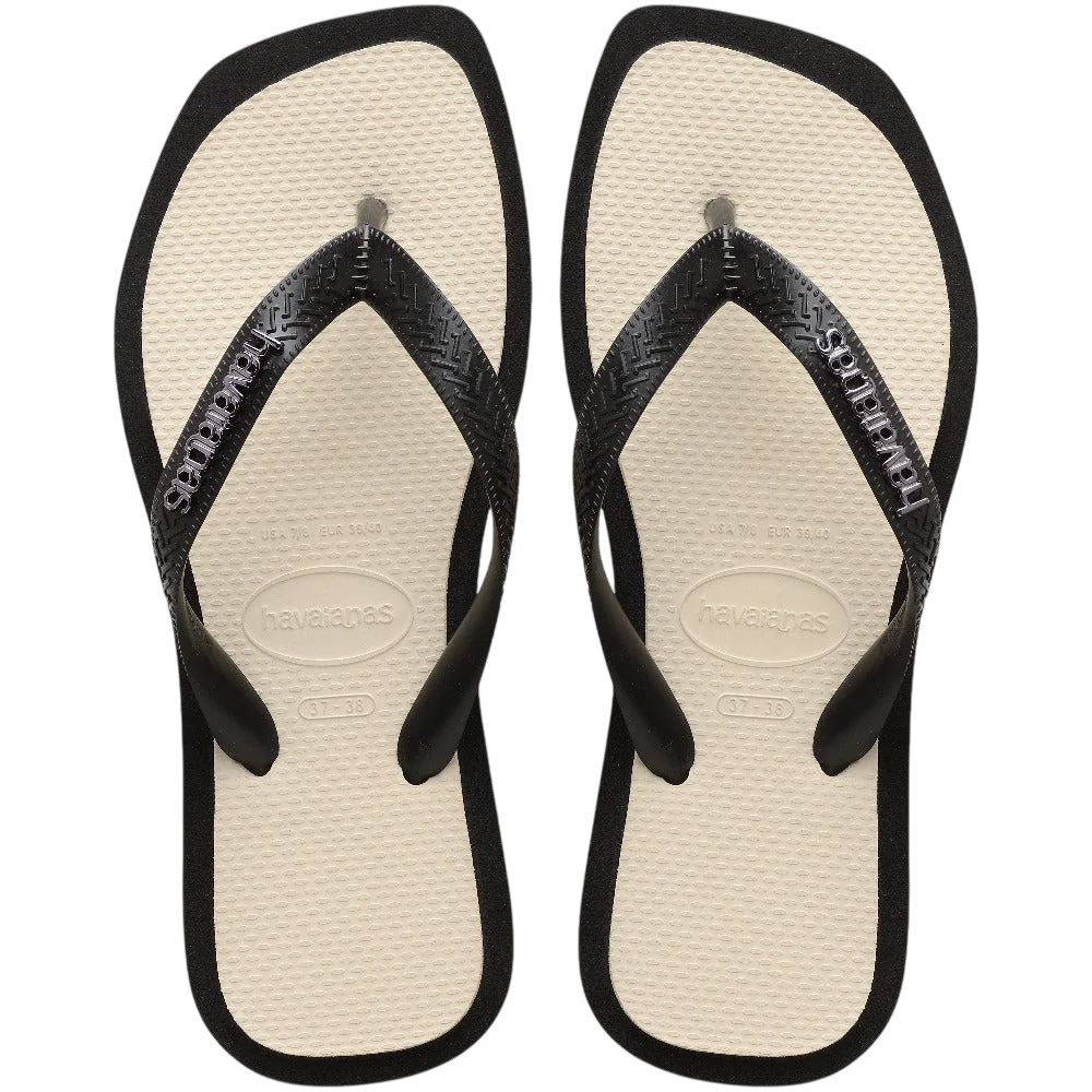 Pair of black and beige Havaianas flip-flops with black straps on a black background.