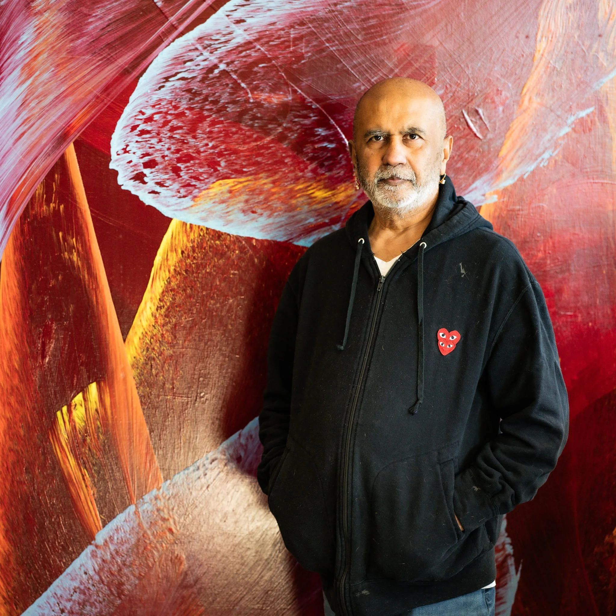 bstract artist Ritu Raj standing in front of an original large-format Organic Movement painting — crimson, sienna, and white — at RituStudio, Phoenix, AZ.