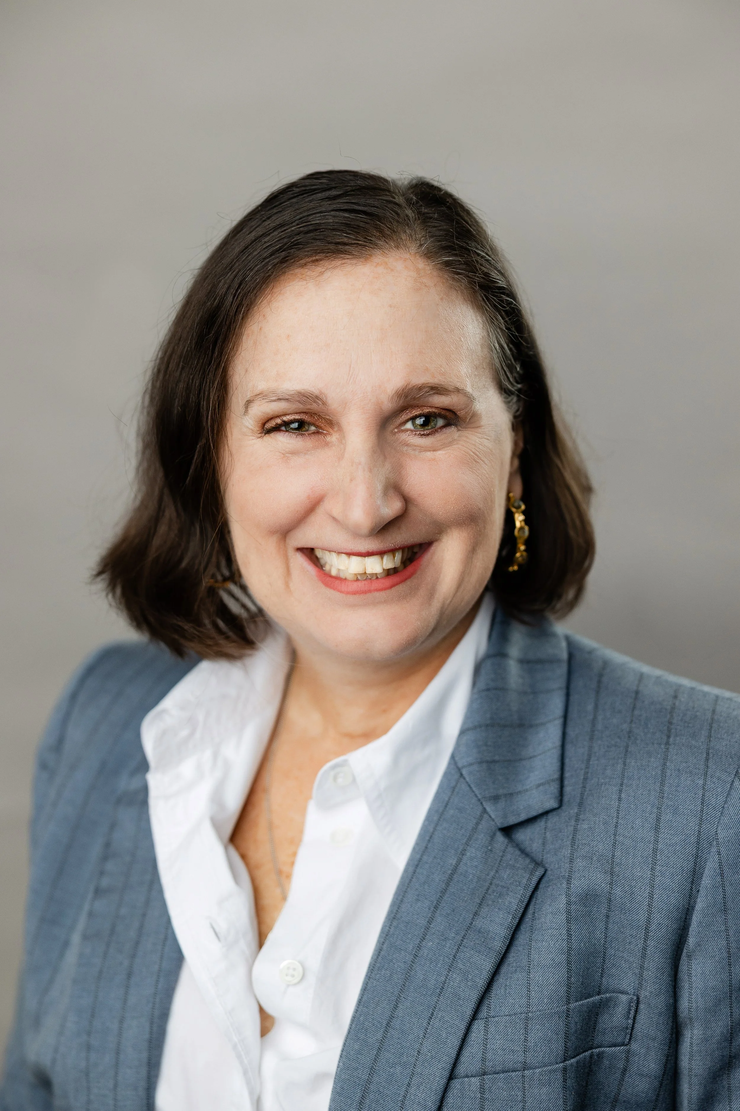 Brunette smiling white woman in slate blue jacket and white blouse
