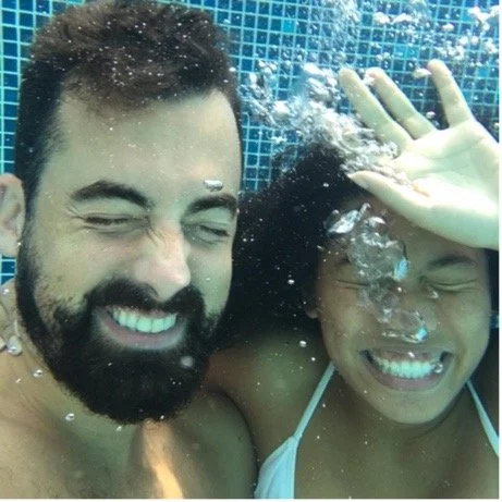 A man and a woman smiling underwater in a pool, posing for a playful selfie.