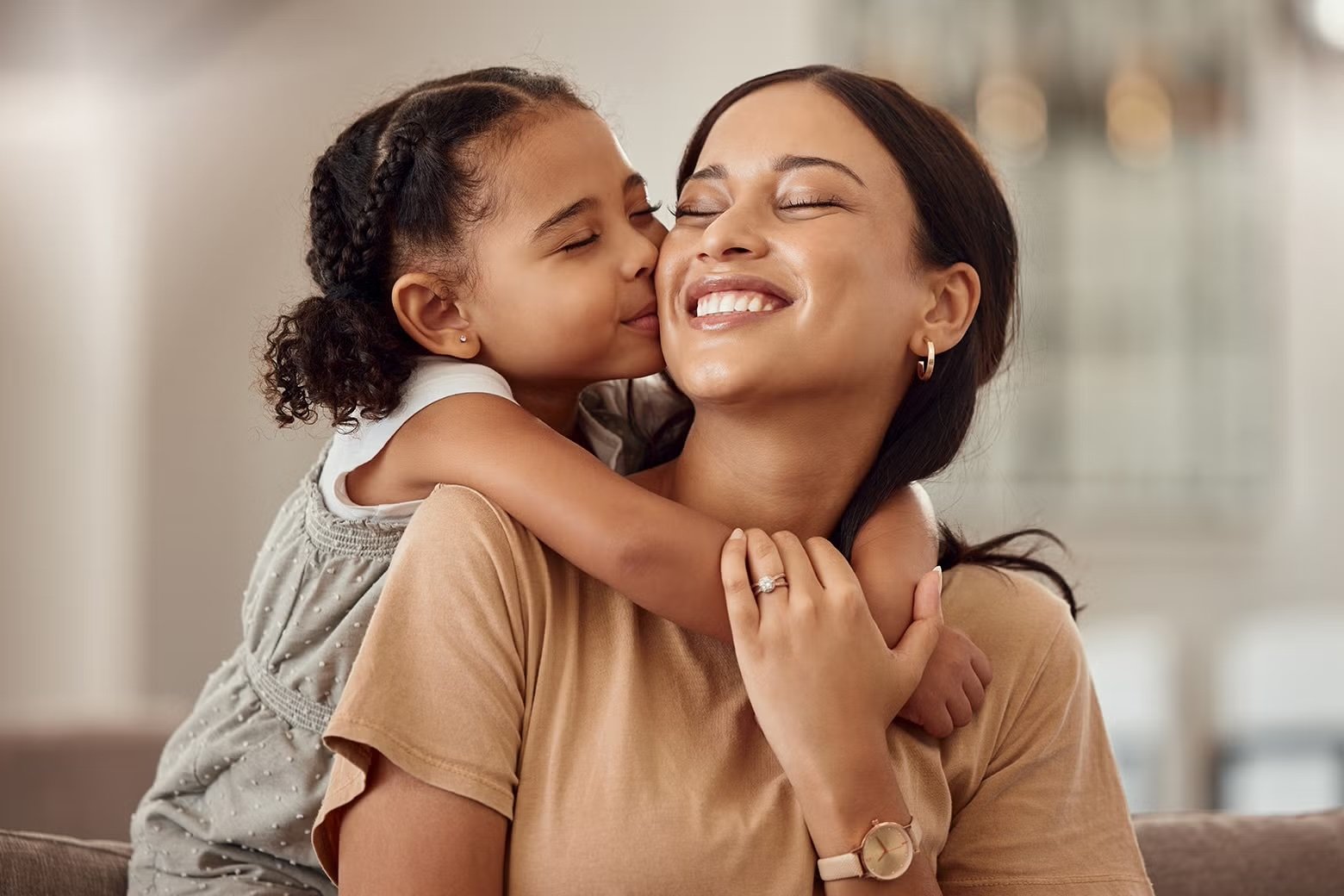 A young girl giving her mother a kiss on the cheek while hugging her.