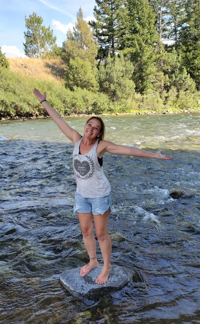 Sarah owner of Inner Wisdom standing on a rock in the Gallatin River outside of Gallatin Gateway. Embrace the joy of your truth.