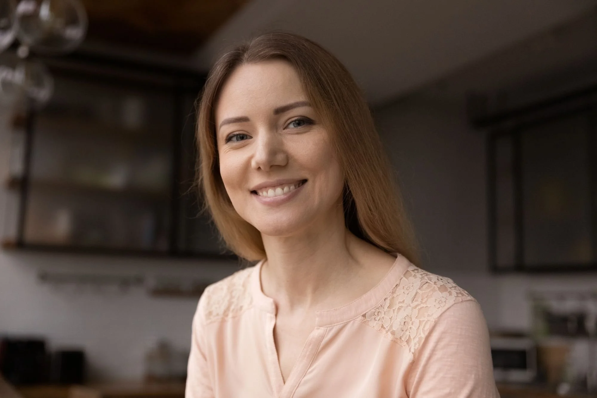 Blonde woman, smiling, sitting in a kitchen. Signs your energy is out of balance indicate that emotional and nervous system healing may help bring your mind body soul and spirit into alignment and you'll begin to hear the signals from inner guidance.