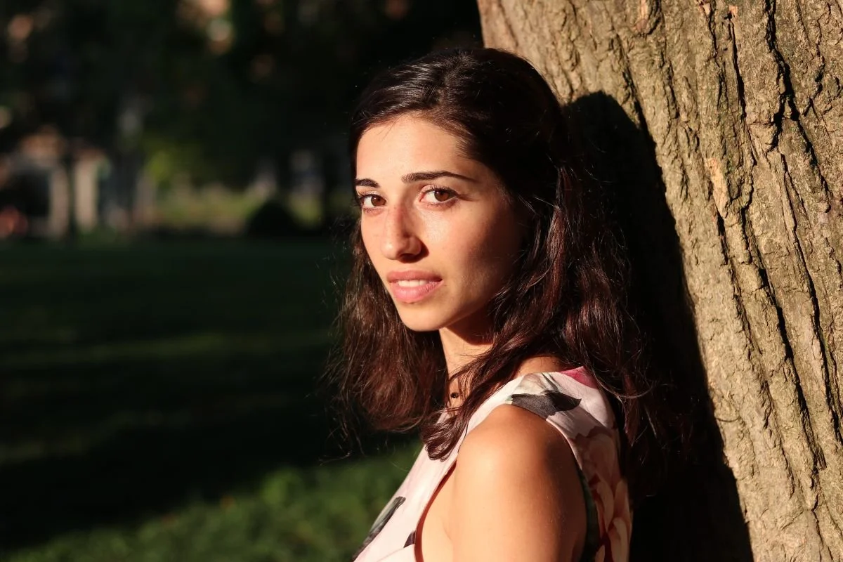 Brown haired women leaning against a tree.  Learn why some conversations stay in your body leading to body tension and emotional residue. When nervous system imprinting keeps conversations trapped in your body you can find yourself weighed down.