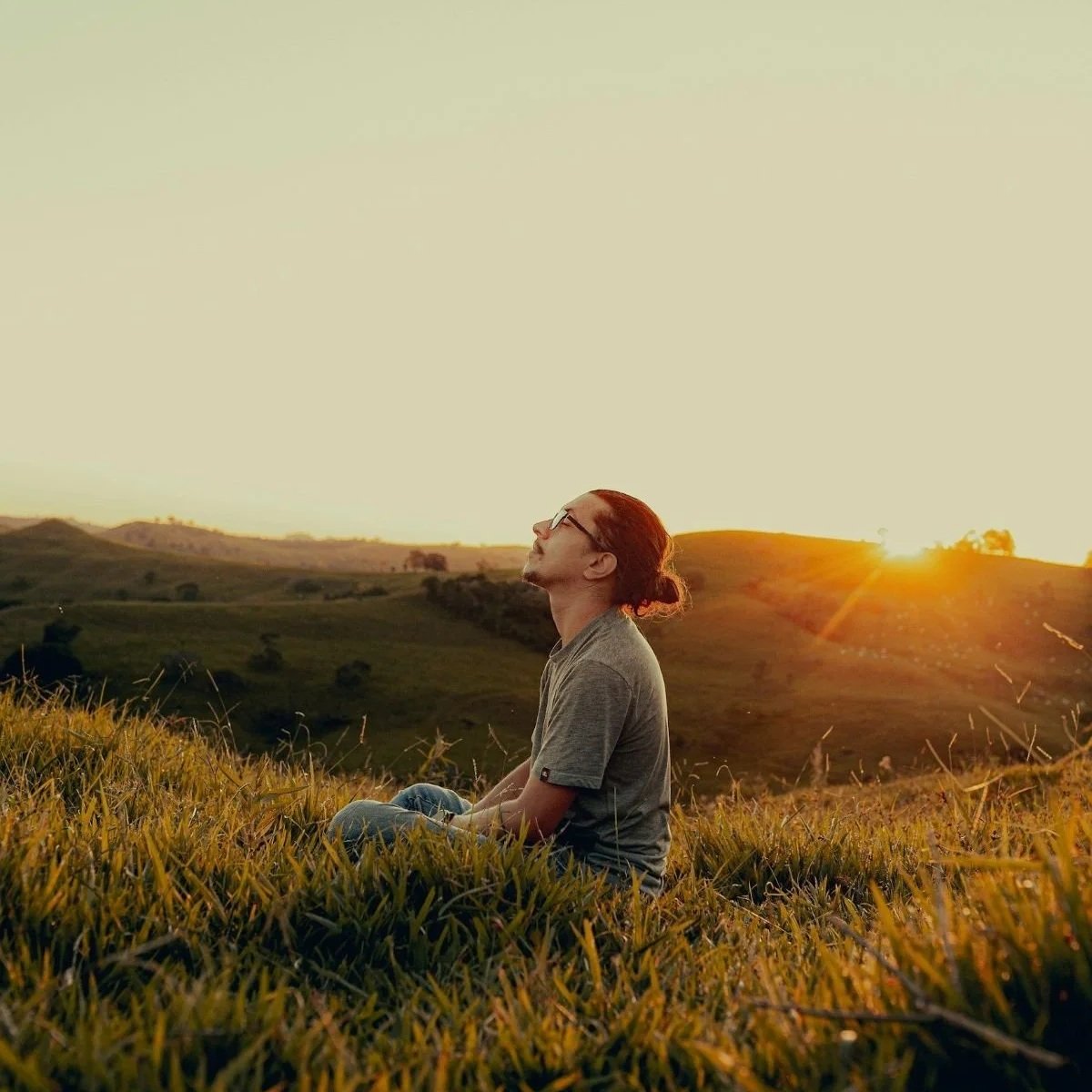 Brown haired man sitting in a field at  sunset. Energy healing and life coaching can help you release long held patterns that keep you in mental loops by resetting your nervous system and working through the psychology that is behind the pattern.