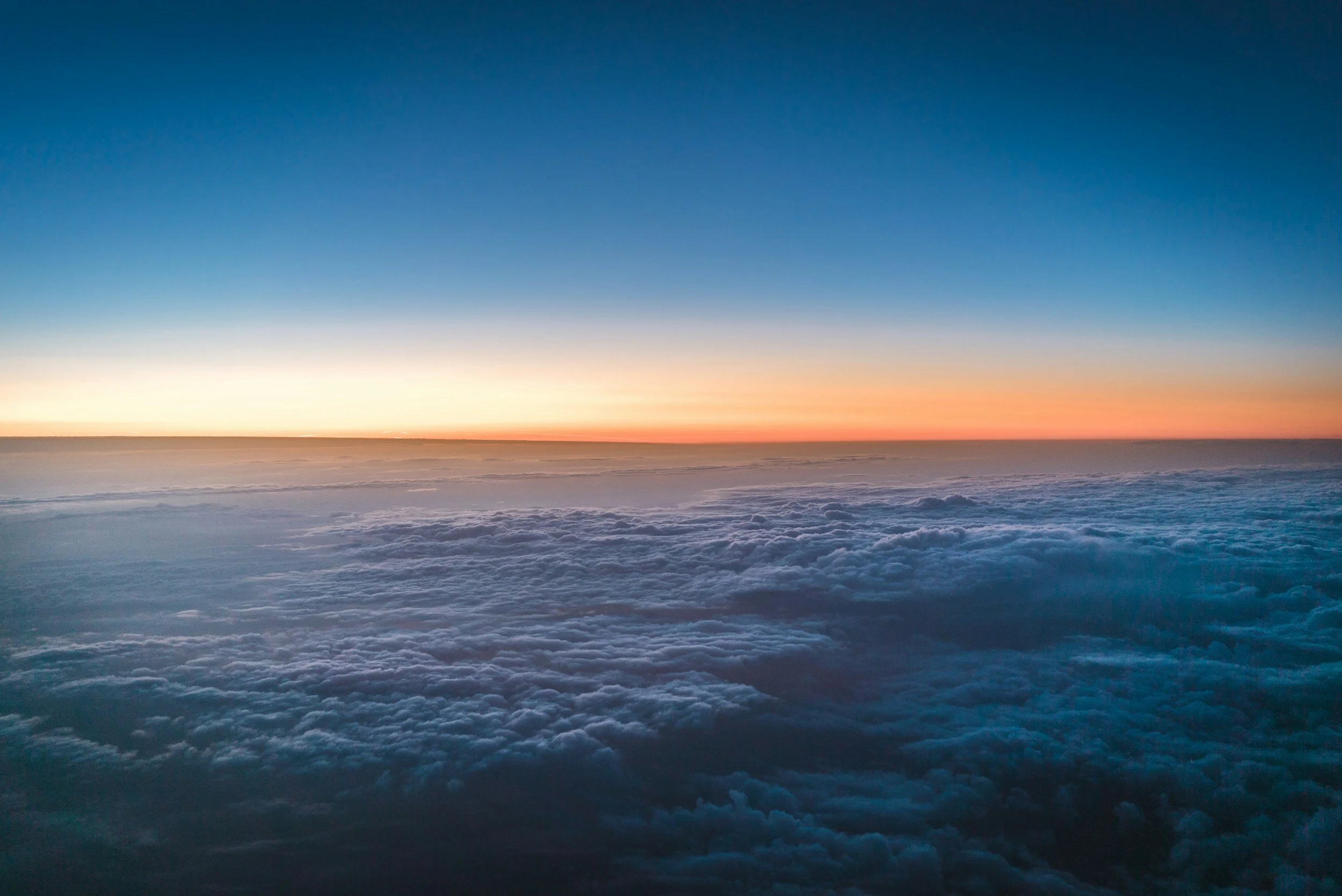 A view of the sky and clouds during sunset or sunrise, with a colorful horizon and a gradient from orange to deep blue.