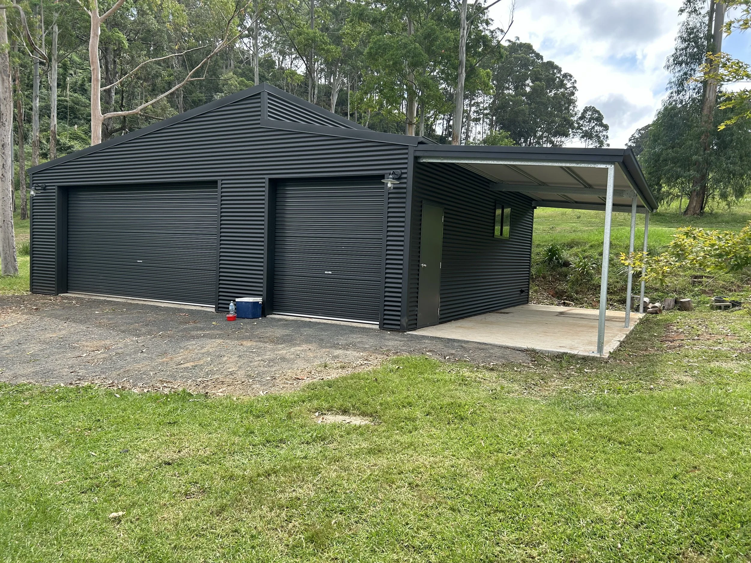 Black shed with 2 roller doors and a verandah attached 
