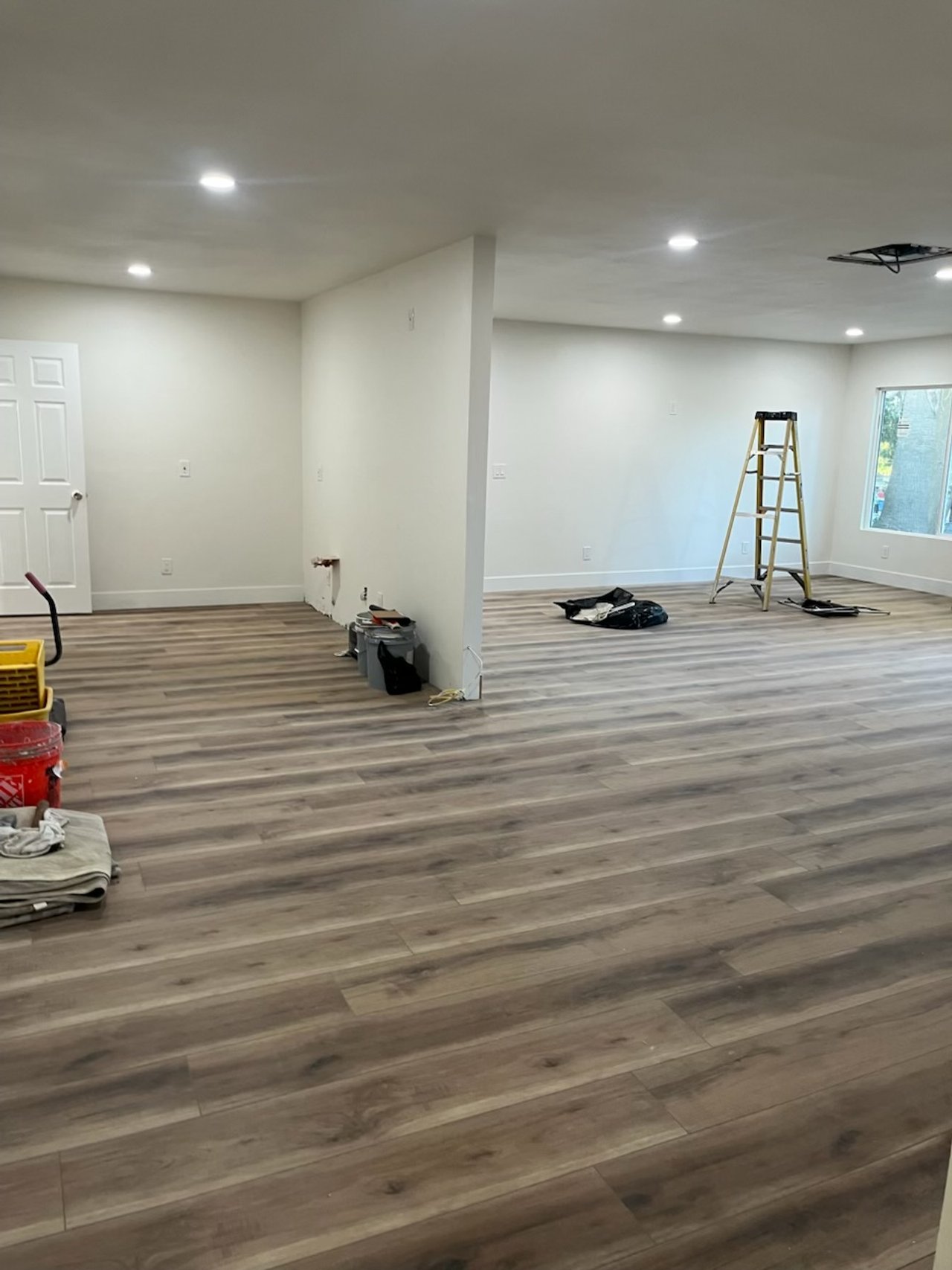 Empty room with wooden flooring, a ladder, construction tools, and a window.
