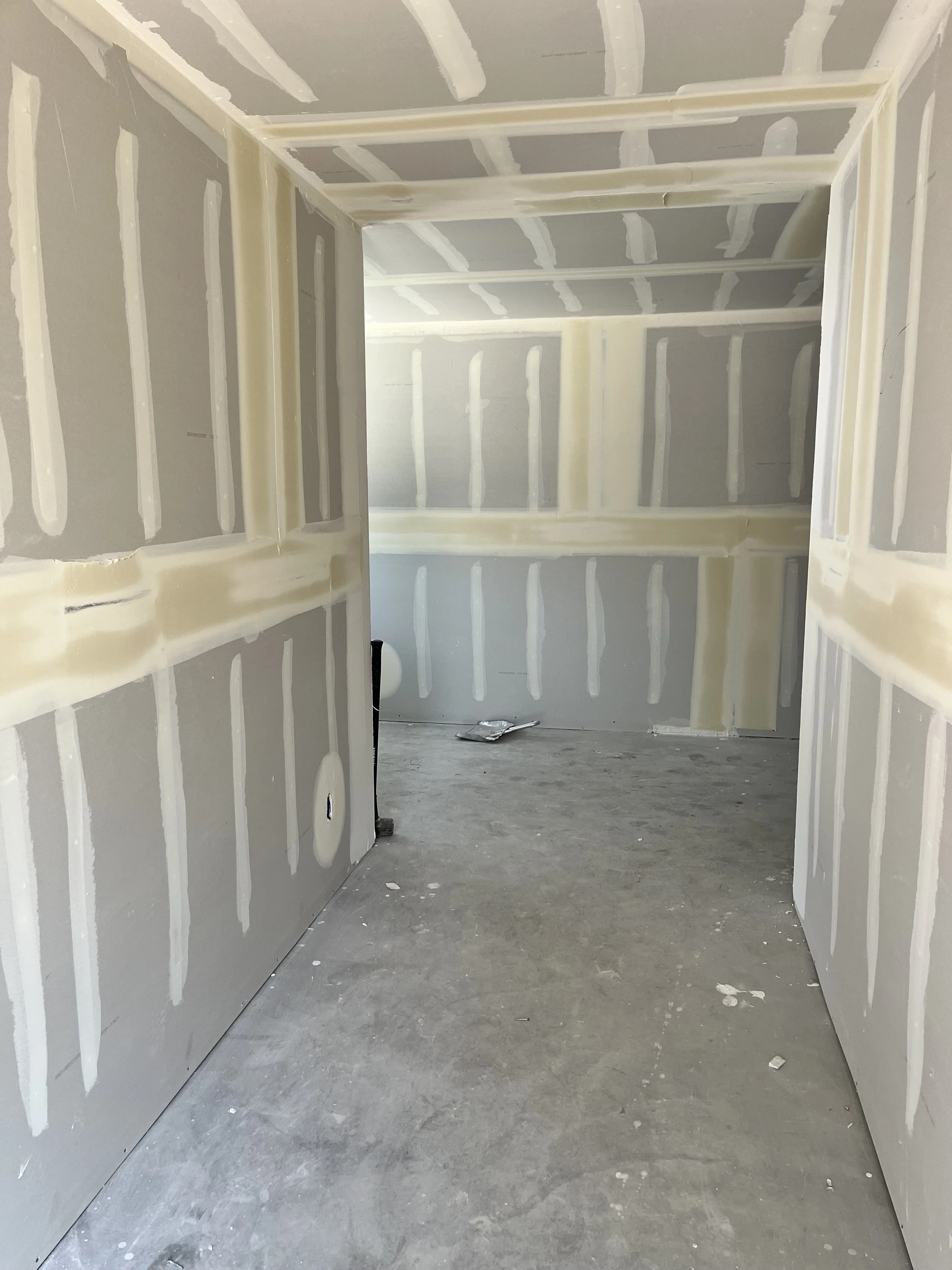 An unfinished room with drywall panels installed and taped, ready for painting or finishing, and a concrete floor.