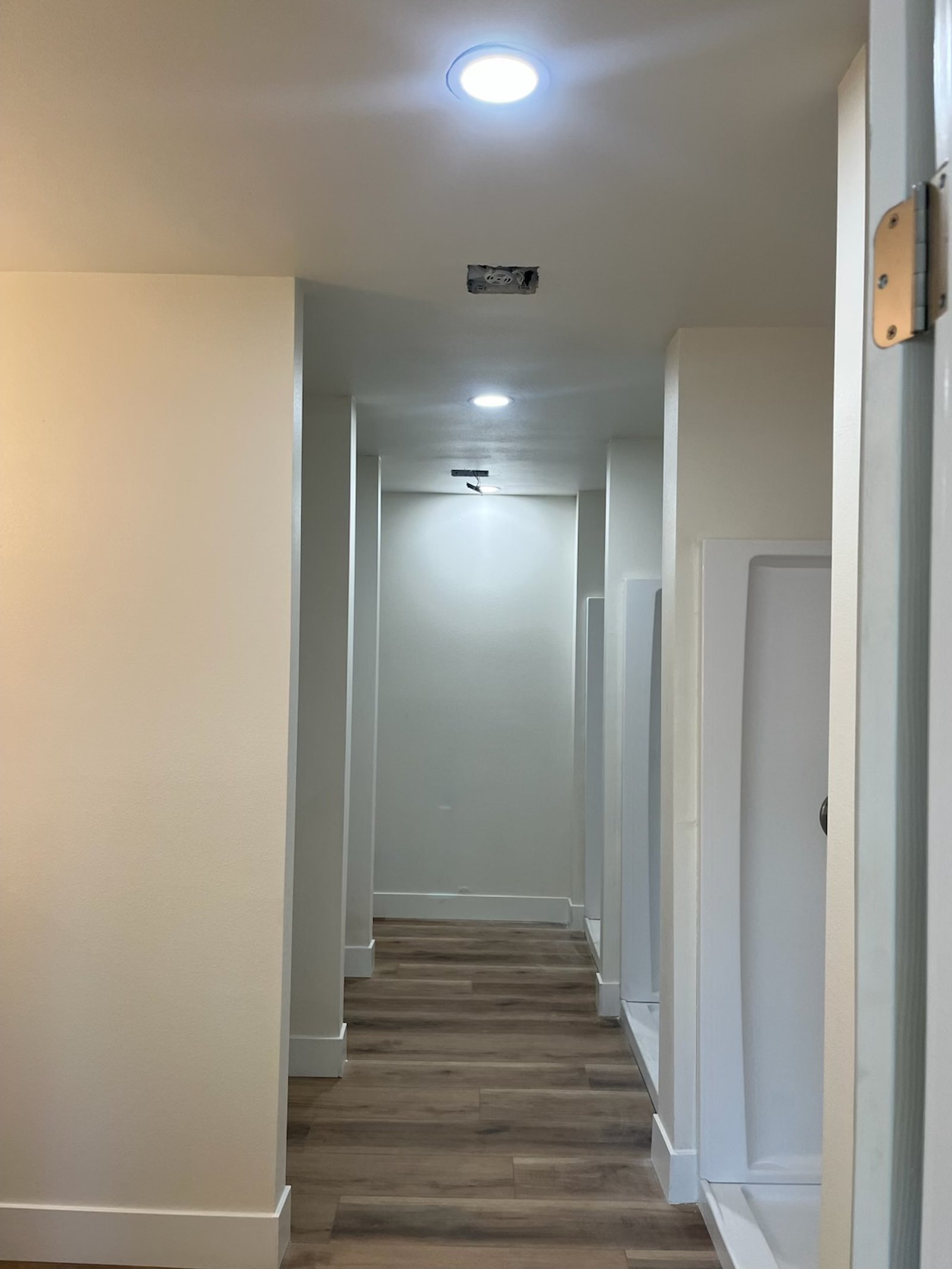 Empty hallway with wooden flooring, white walls, and multiple ceiling lights, some of which are not yet installed.