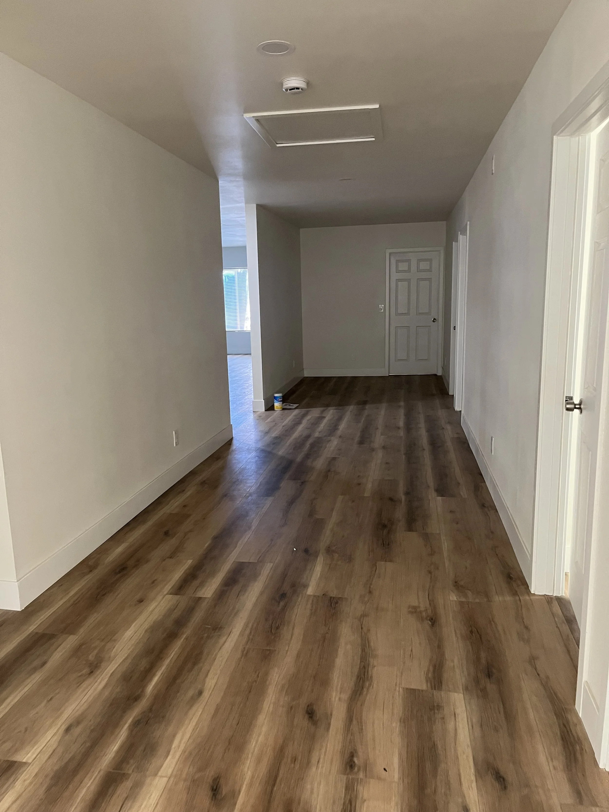 Empty room with wooden flooring, white walls, ceiling light fixture, and a closed door in the background.