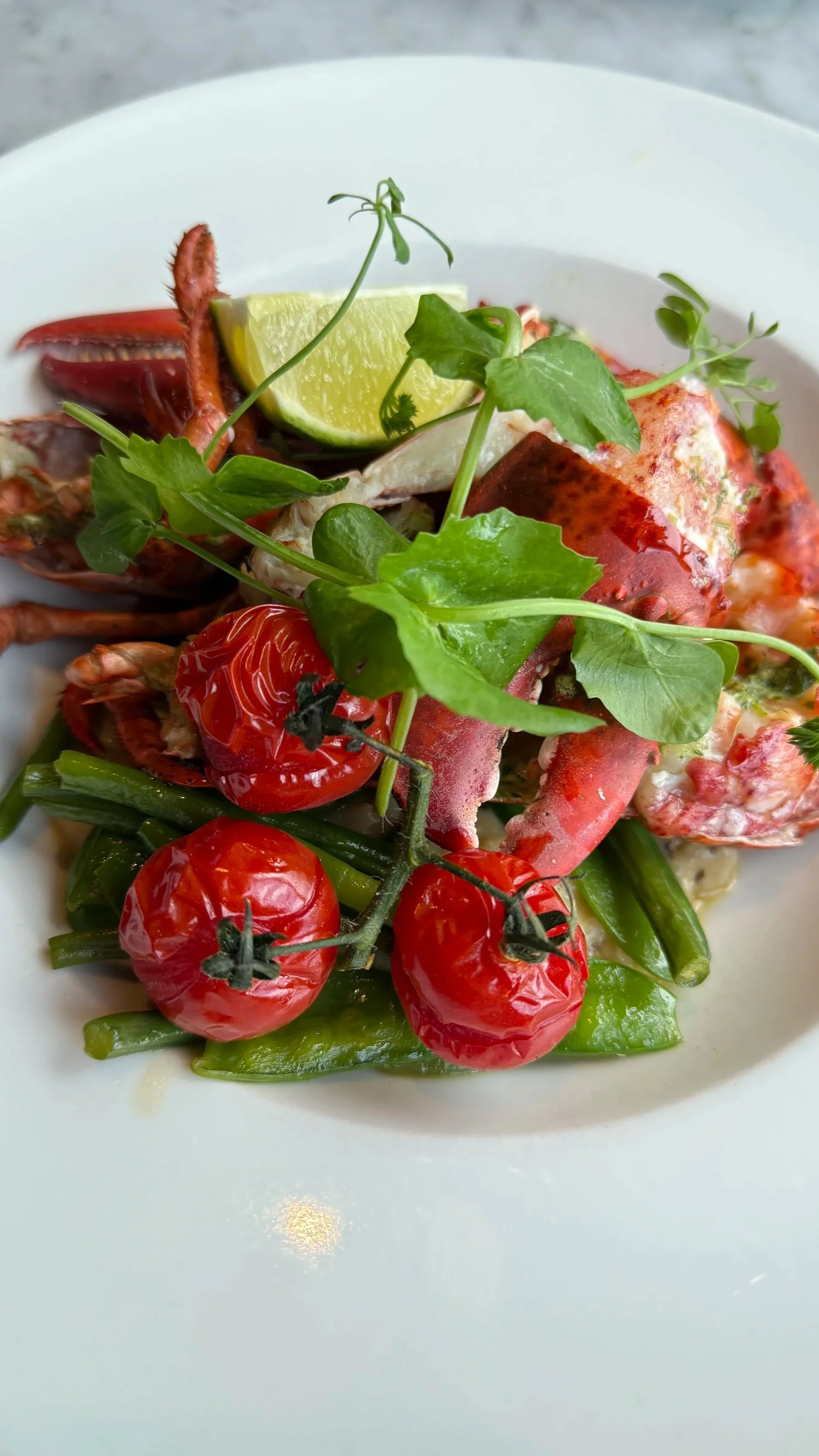 Lobster dish garnished with cherry tomatoes, lime wedge, and fresh herbs, served on a white plate.
