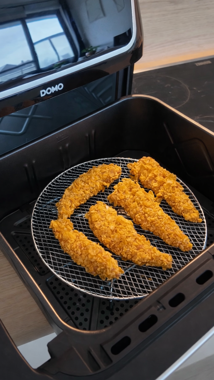 Six breaded chicken tenderloins in an air fryer basket.