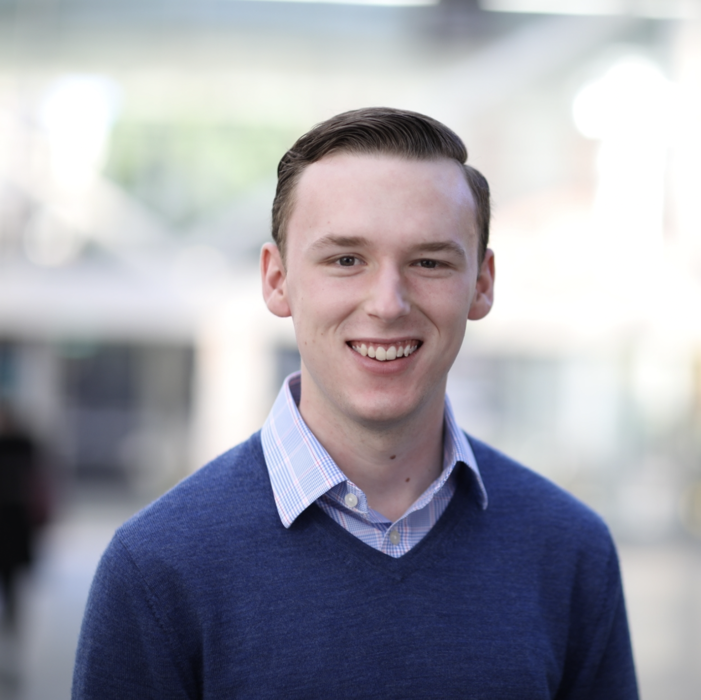 Smiling person in a blue sweater and collared shirt, blurred background