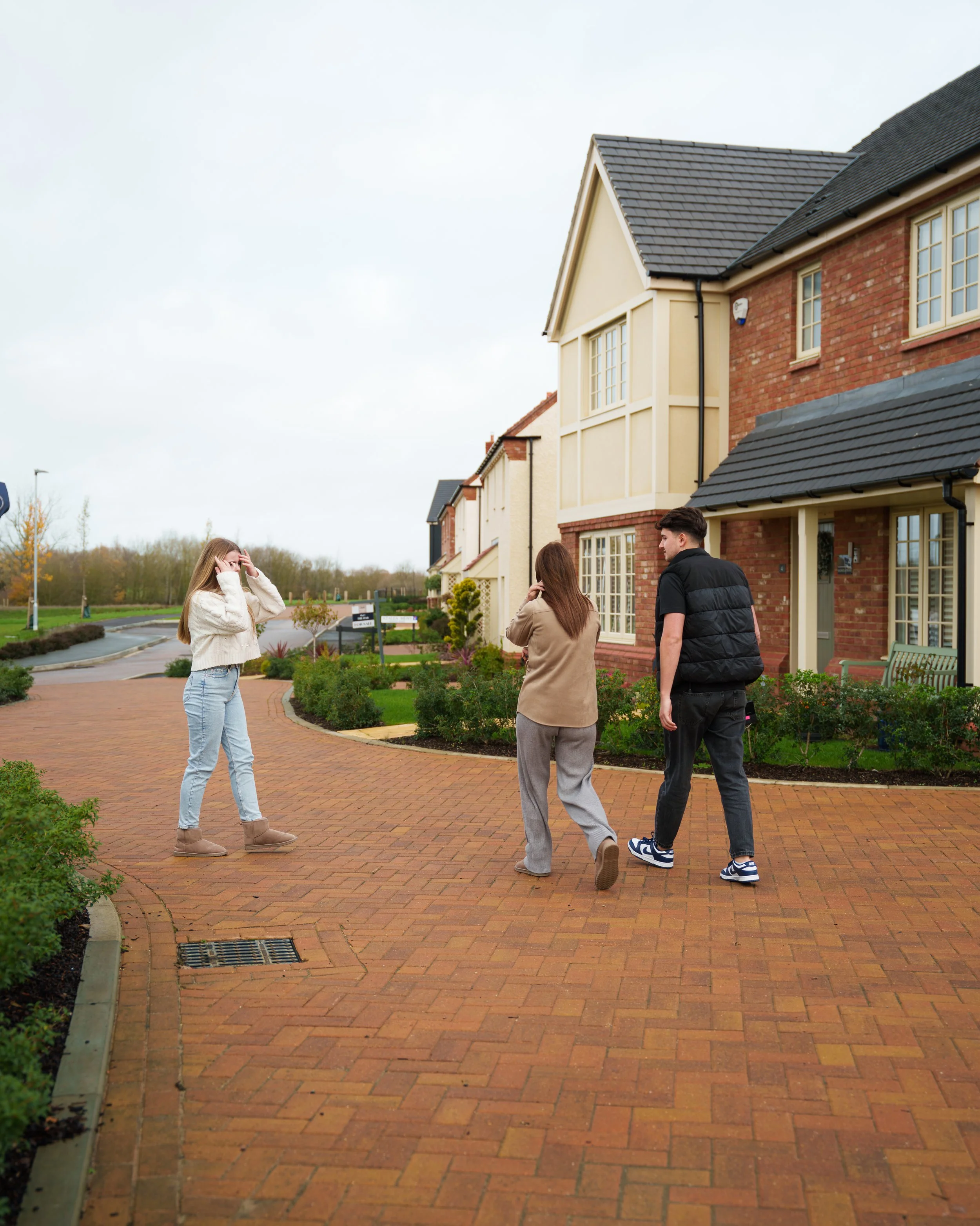 Three people walking on a brick sidewalk in front of a row of townhouses, with one woman standing apart and two walking together.