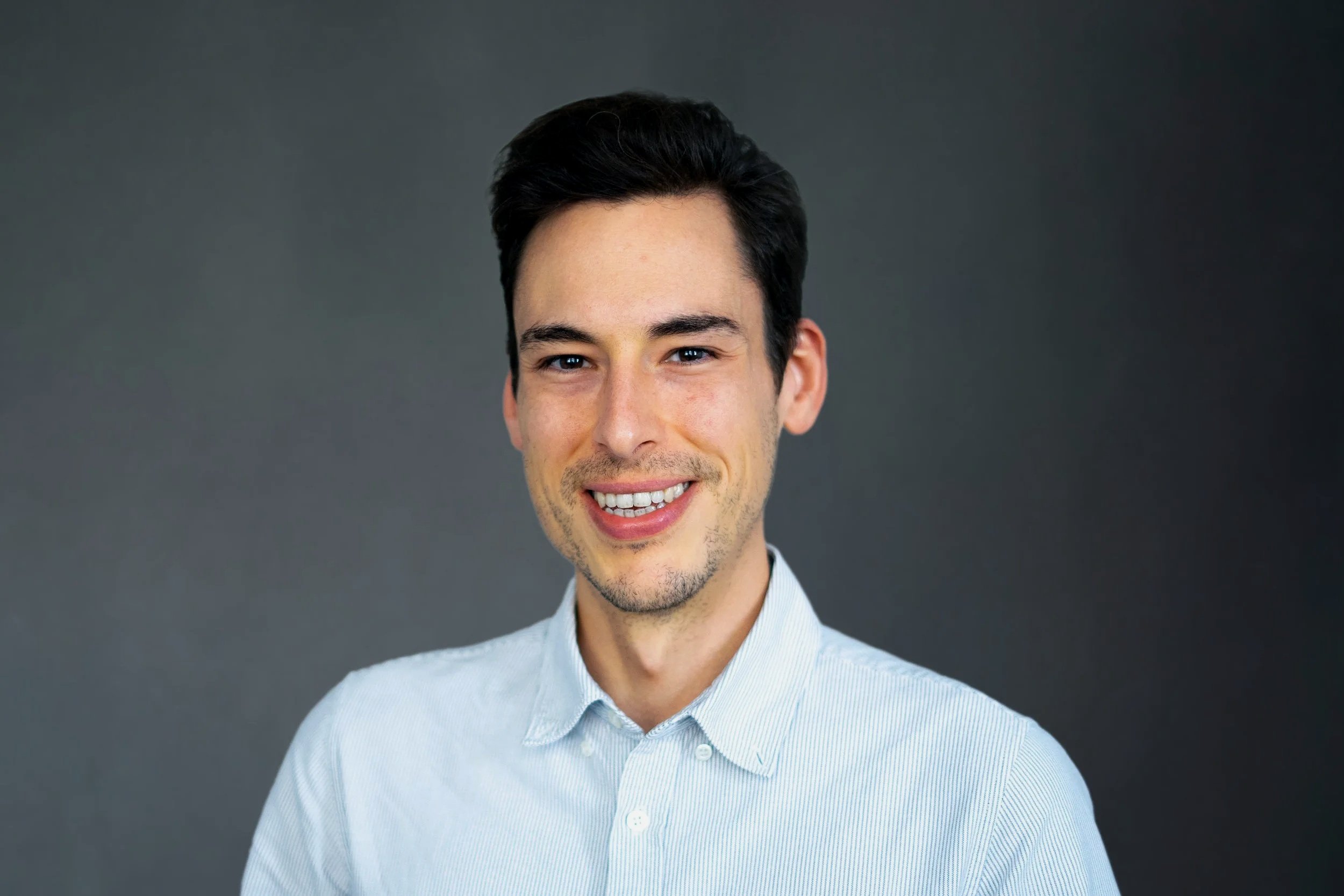 A profile picture of a digital designer smiles at the camera in a white shirt