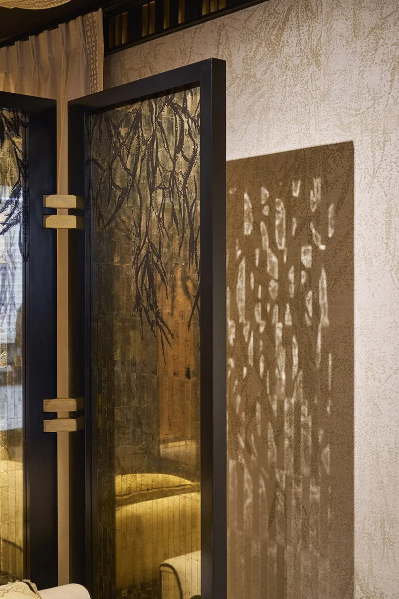 Une cloison avec un cadre noir et des motifs en moucharabieh, créant une ombre complexe sur le mur à côté.