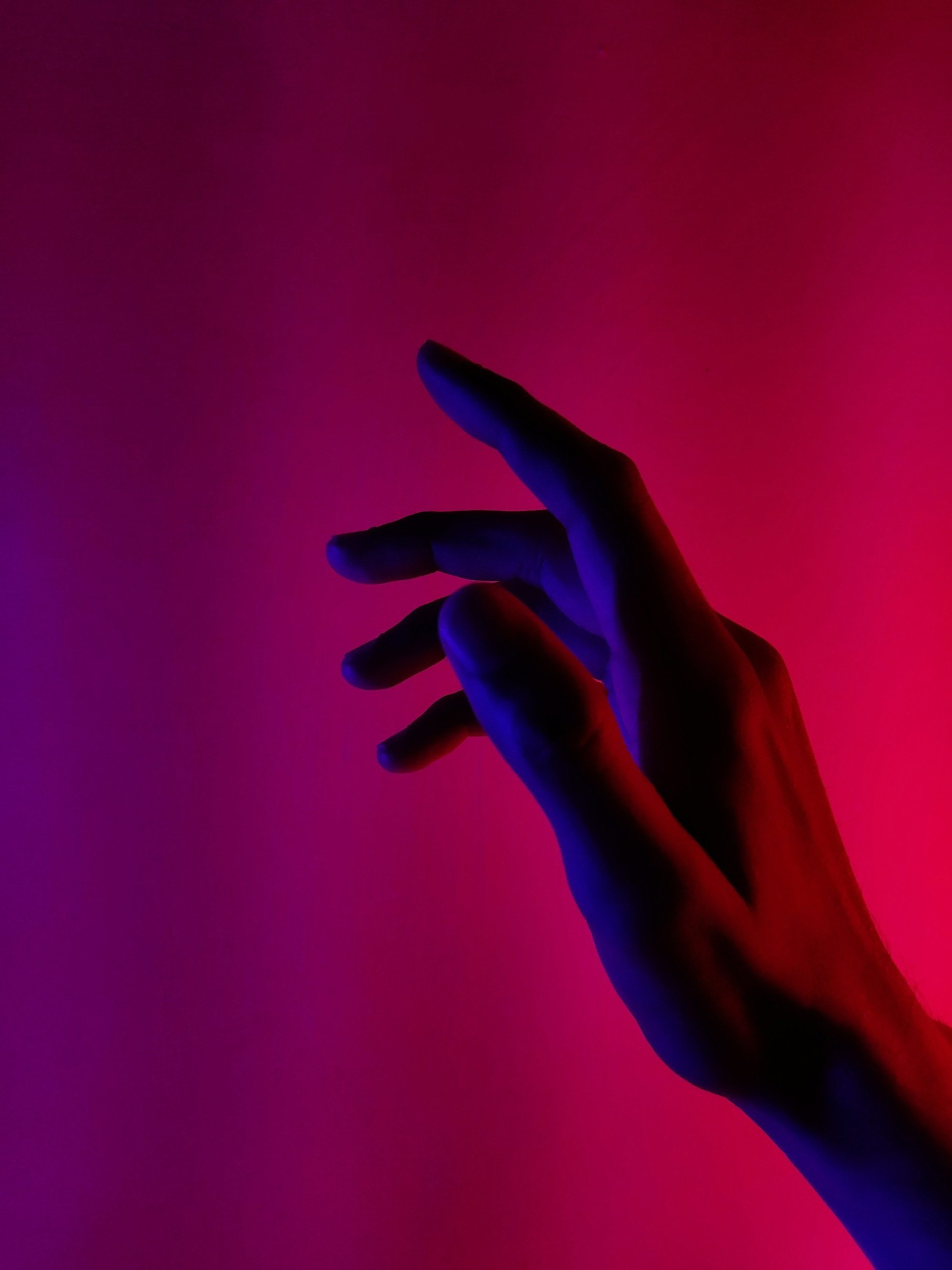 Main humaine en silhouette noire contre un fond rouge et violet, éclairée par une lumière bleue et rouge.