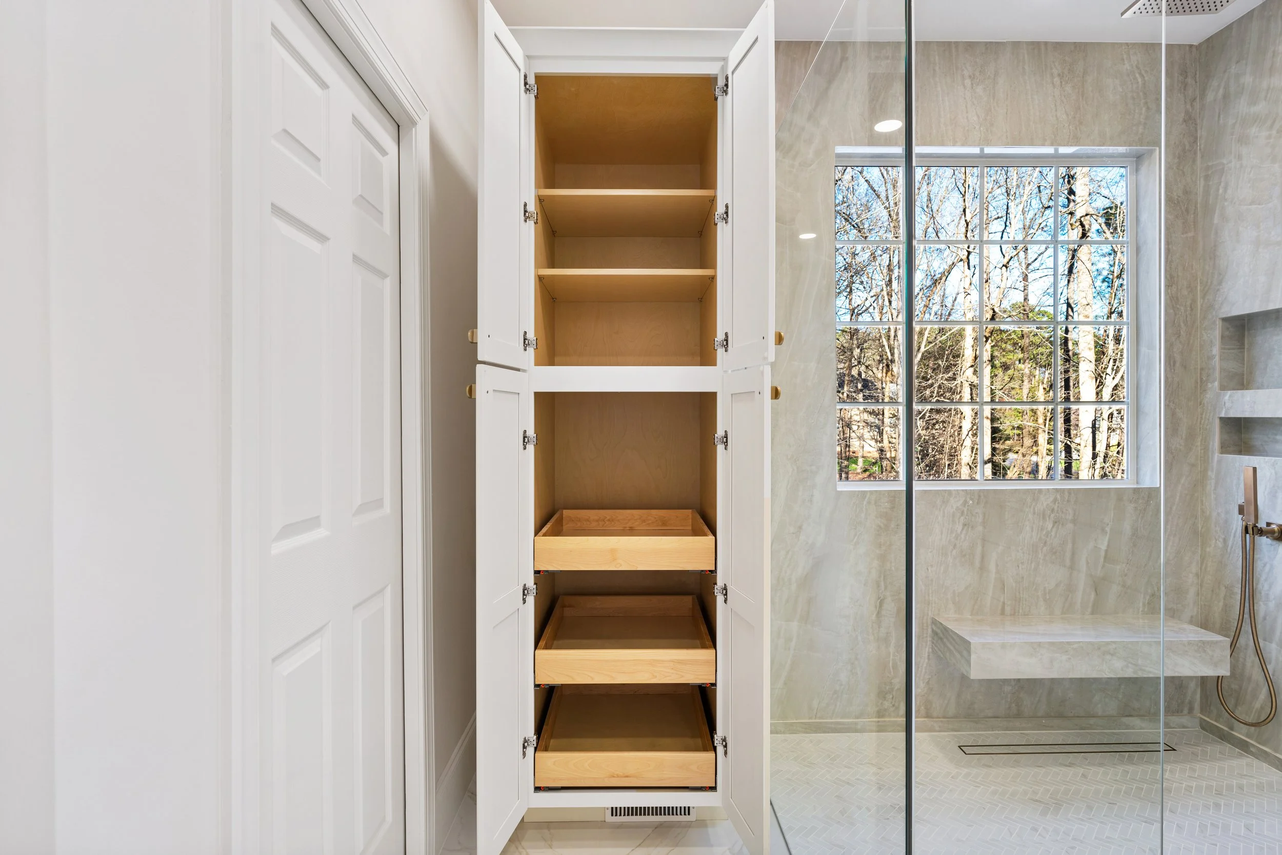 Bathroom with a built-in storage cabinet and a walk-in shower with a large window and marble walls.