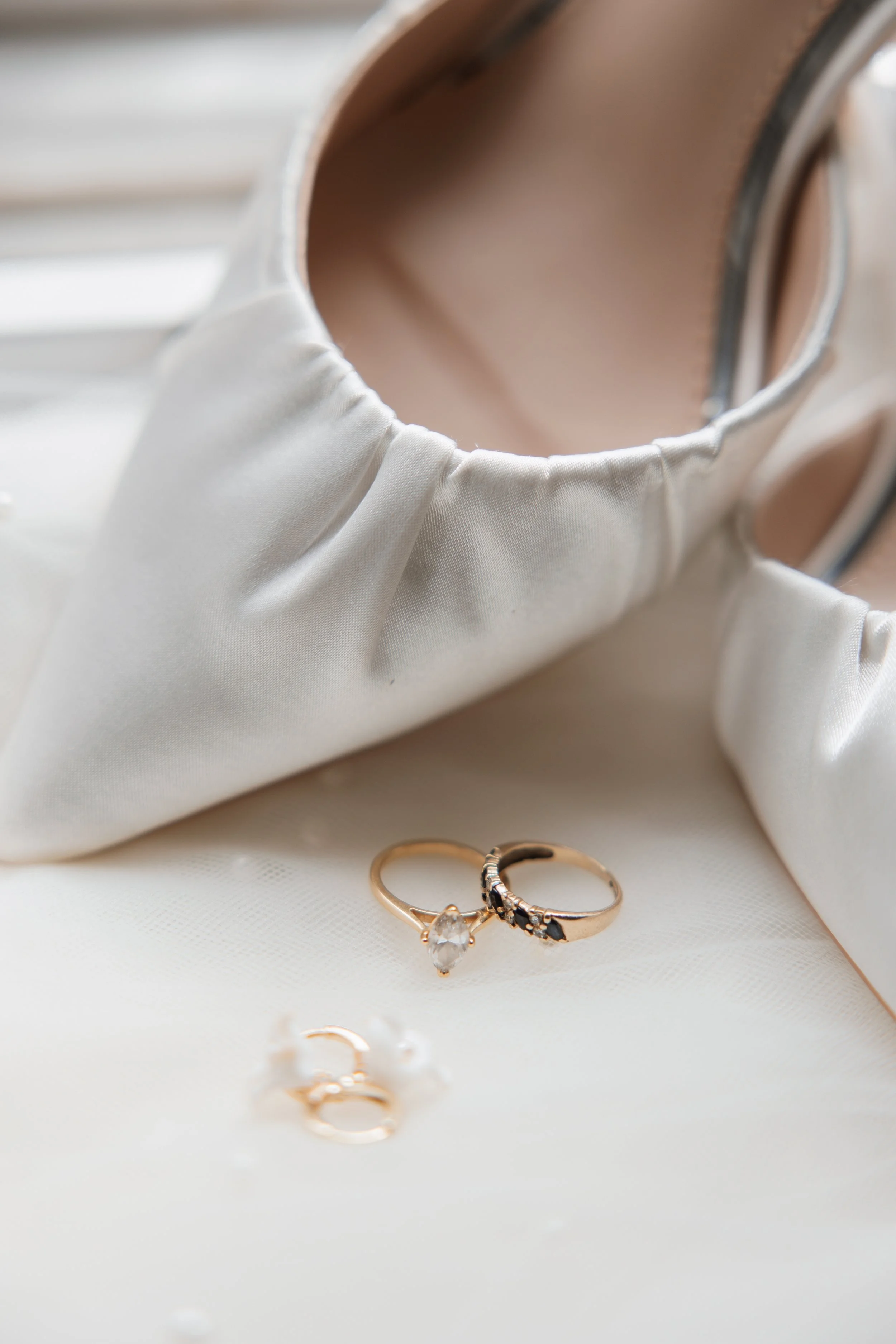 Close-up of two gold rings, one with a large gemstone and the other with black stones, on white fabric with a satin pouch in the background.
