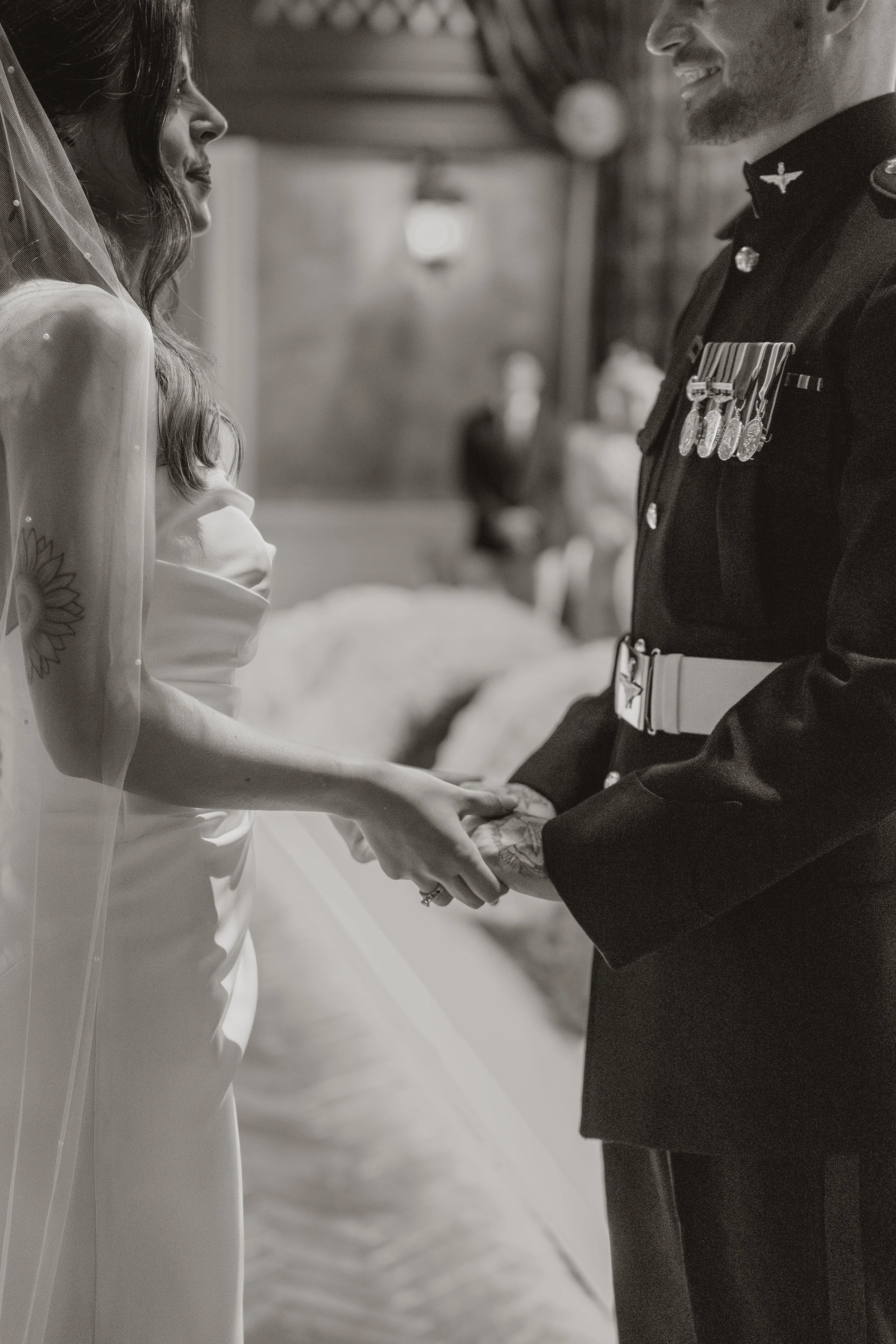 A bride and groom holding hands during their wedding ceremony, both smiling, in a black and white photo.