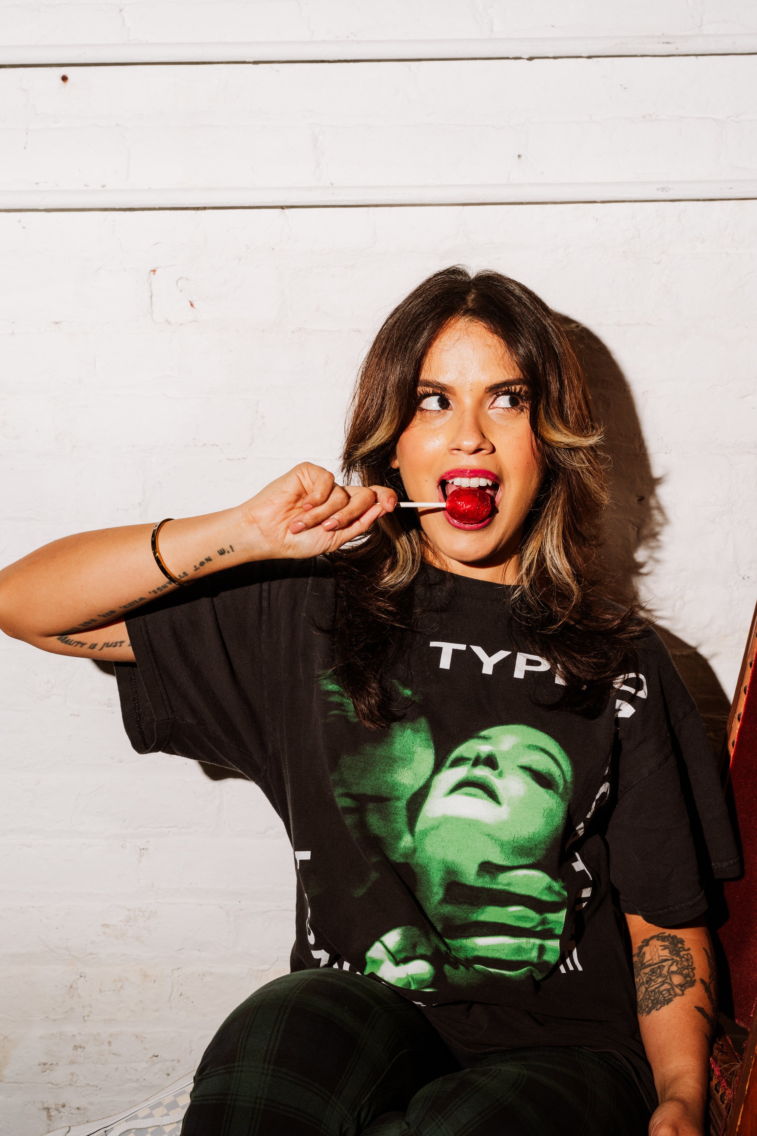 Portrait of woman with lollipop and graphic t-shirt against white wall, editorial photography New Jersey