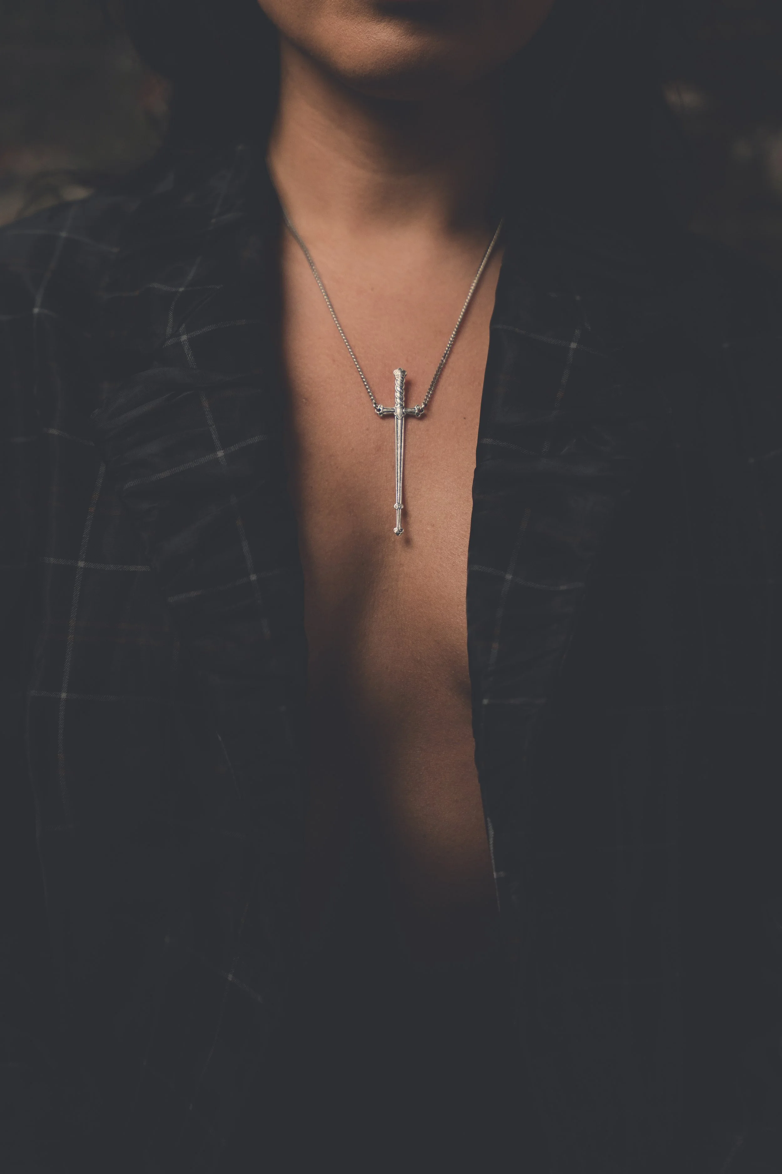 Moody portrait detail of necklace and blazer in low light, cinematic editorial photography