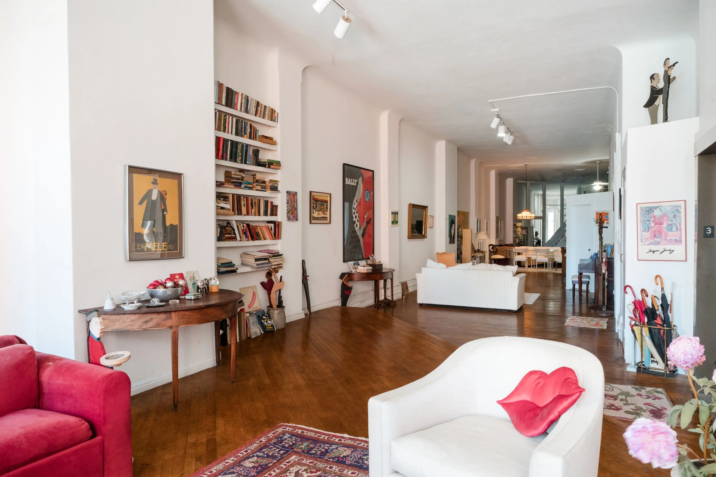 Bright Greenwich Village loft living room with red sofa, Persian rug, and folk-art tray figures.