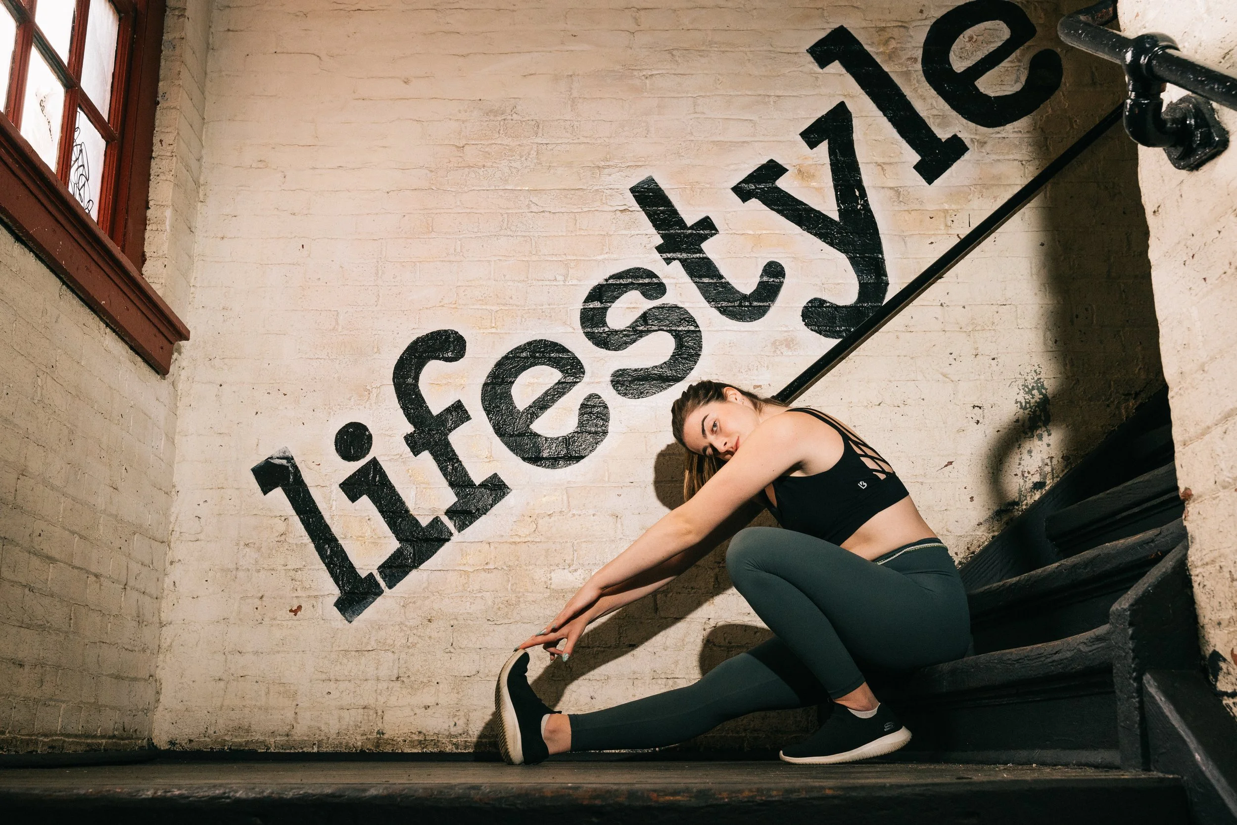 Editorial portrait of woman stretching on staircase under “Lifestyle” sign, Art Factory Paterson NJ