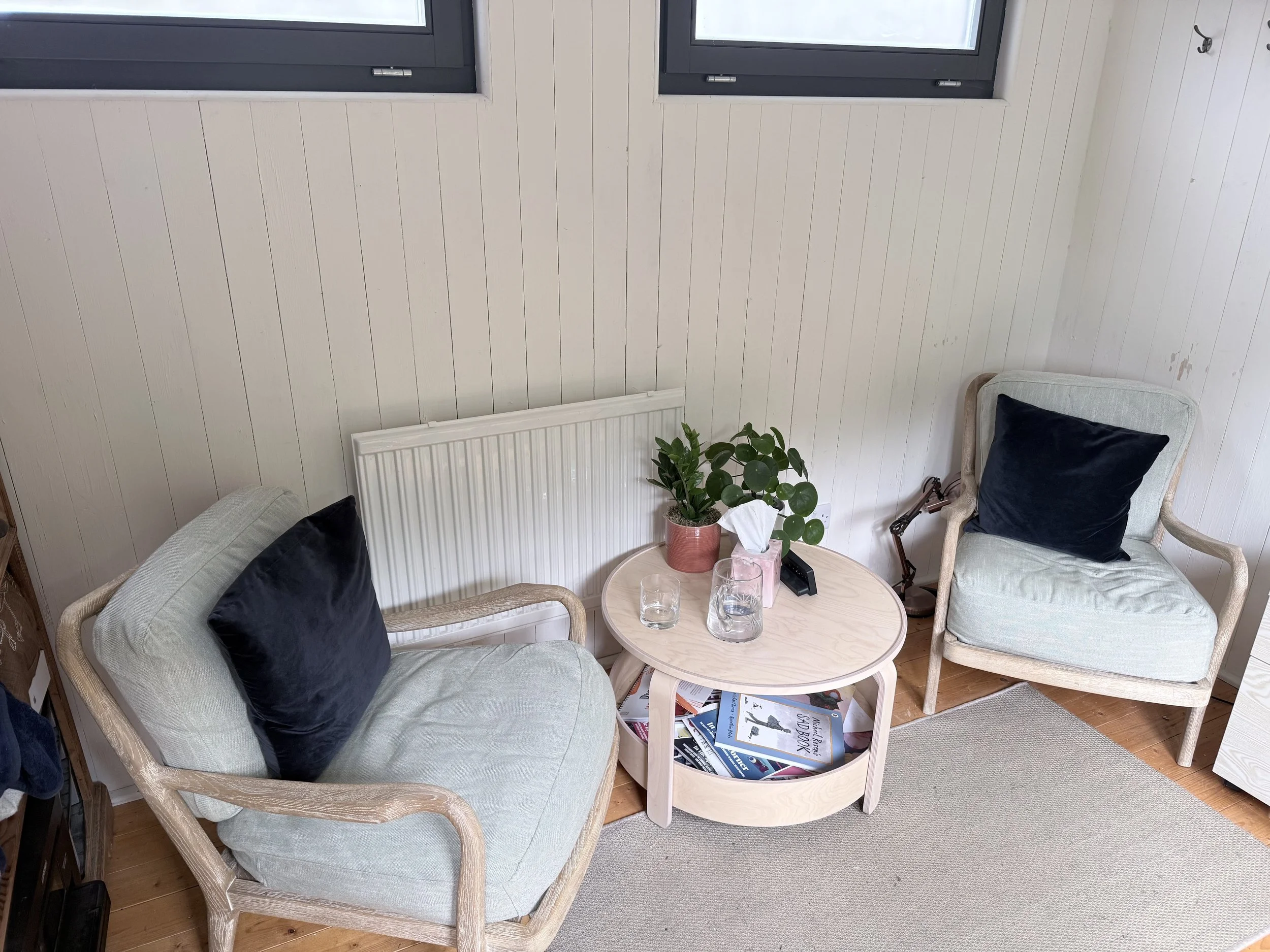 Two comfy chairs and a table in the middle with tissues and water