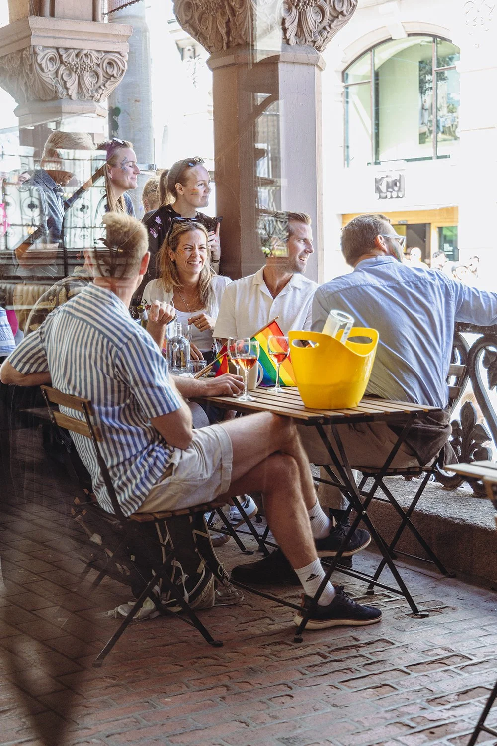 En gruppe mennesker som koser seg på Pride, med flagg og god drikke i glassene