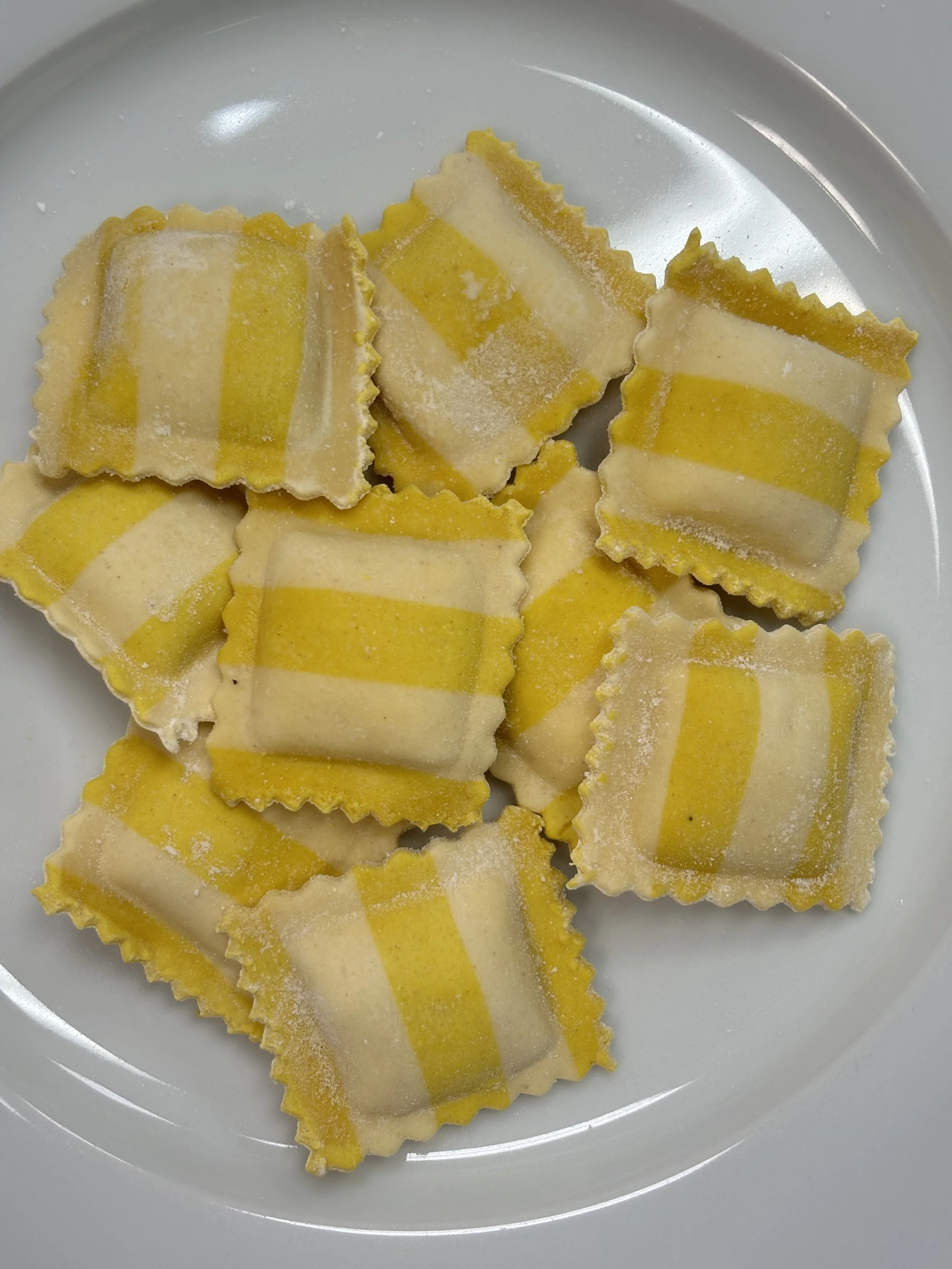 Close-up of yellow and white striped ravioli pasta on a white plate.