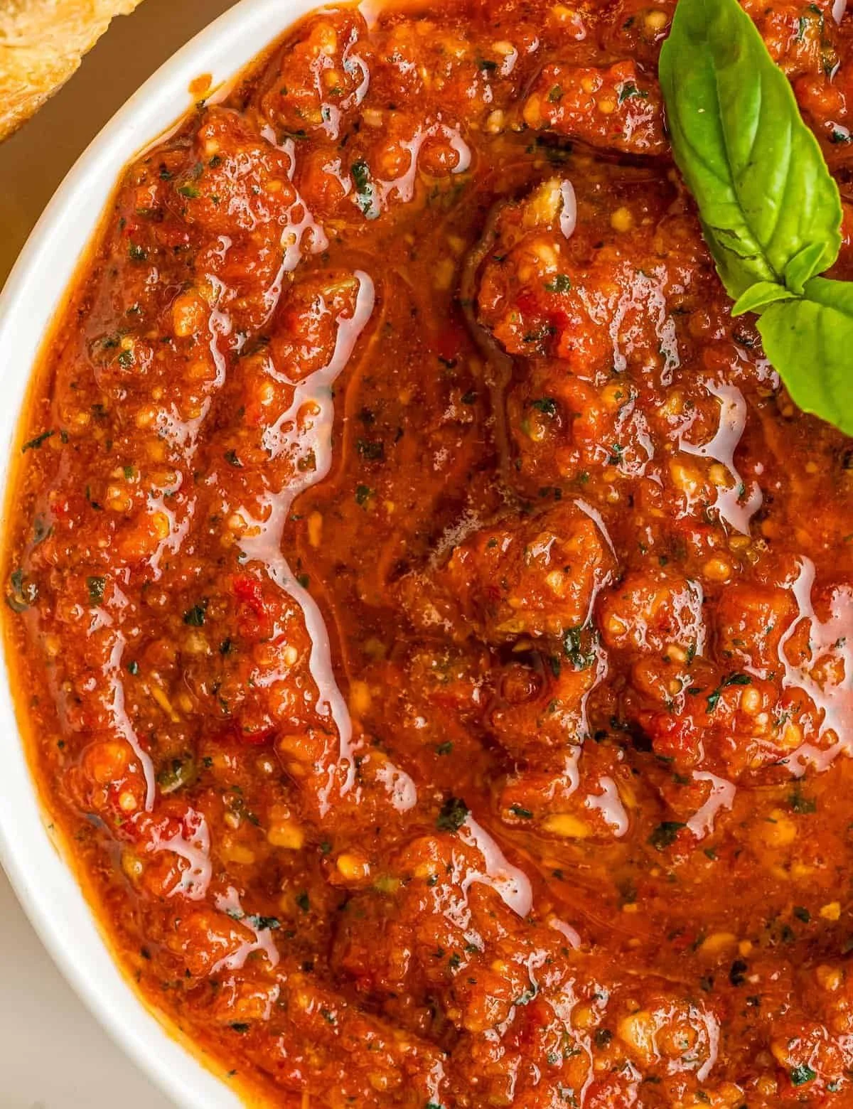 Close-up of a bowl of spicy meatball stew garnished with fresh basil leaves.