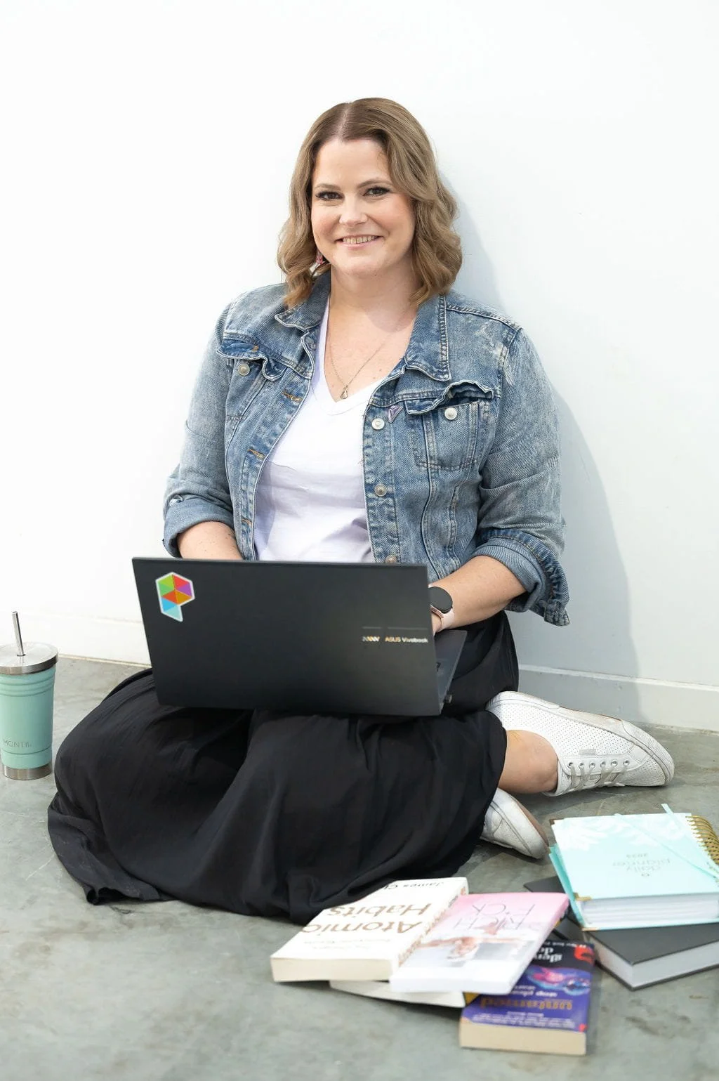 Squarespace website designer Janelle Strickland. She is sitting on the floor with a laptop on her lap, wearing white sneakers, a black skirt, a lilac top and a demin jacket.