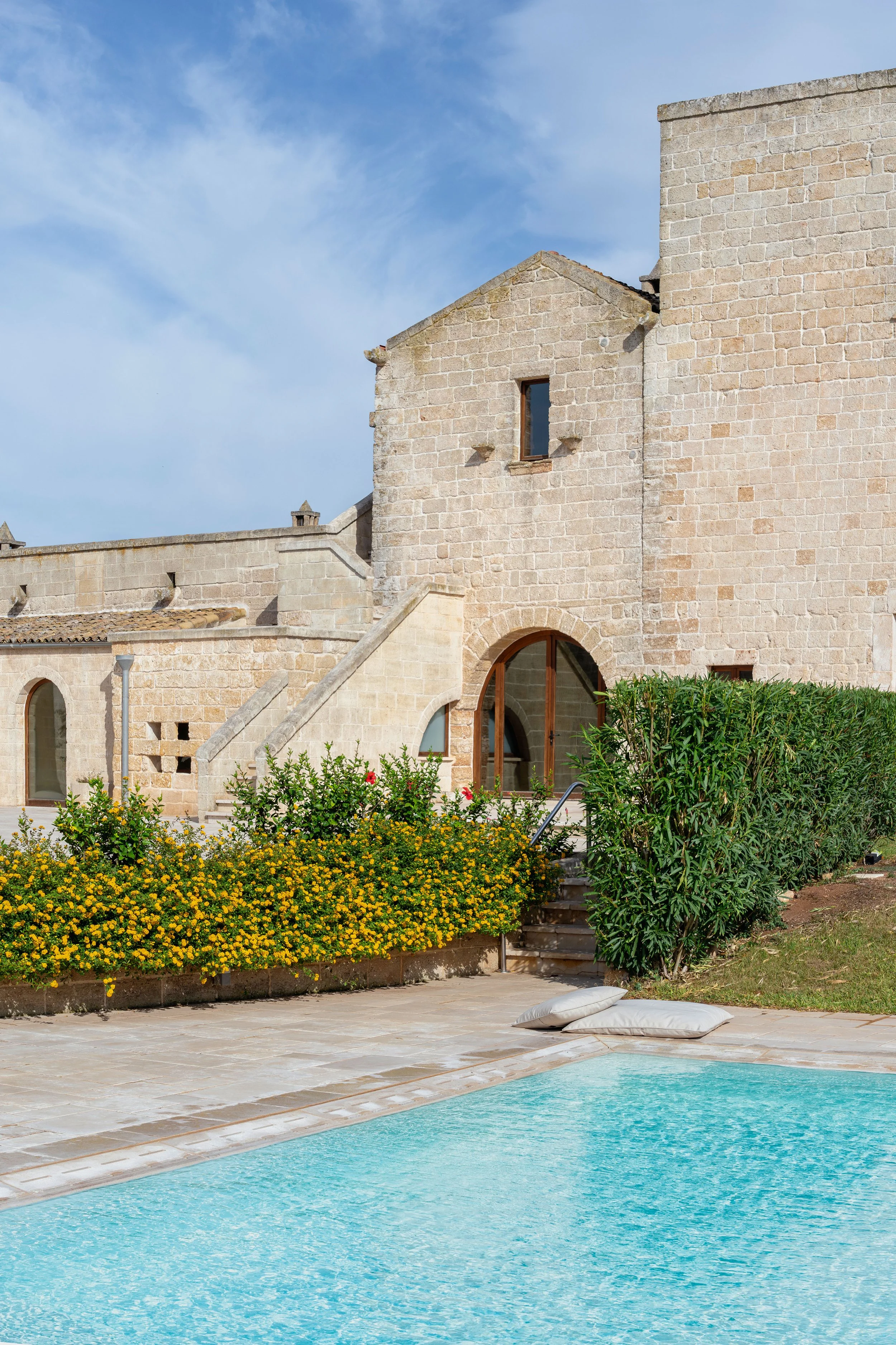 Historic stone building with arched windows next to a swimming pool and garden