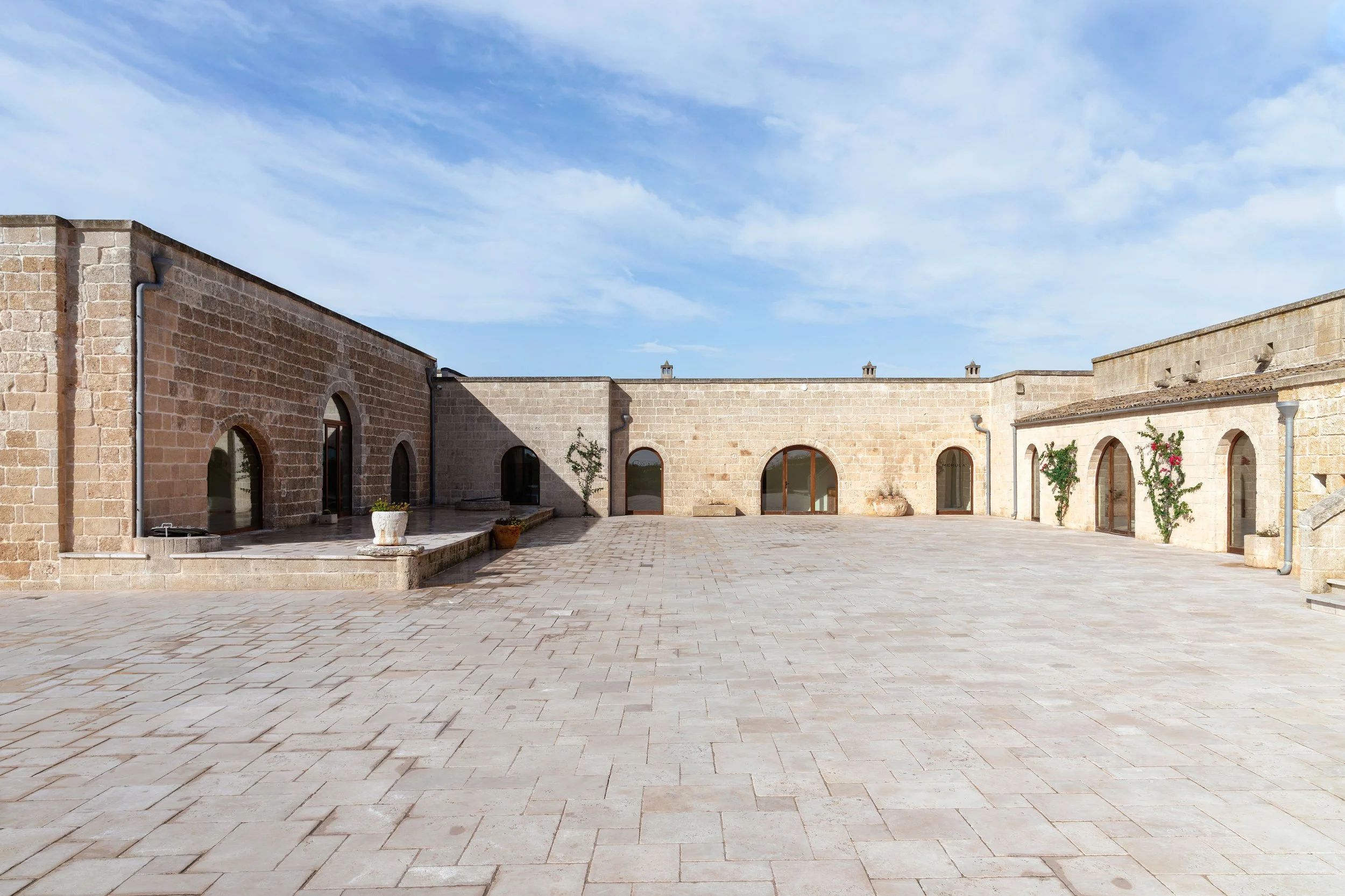 Stone courtyard with arched doorways, potted plants, clear sky.